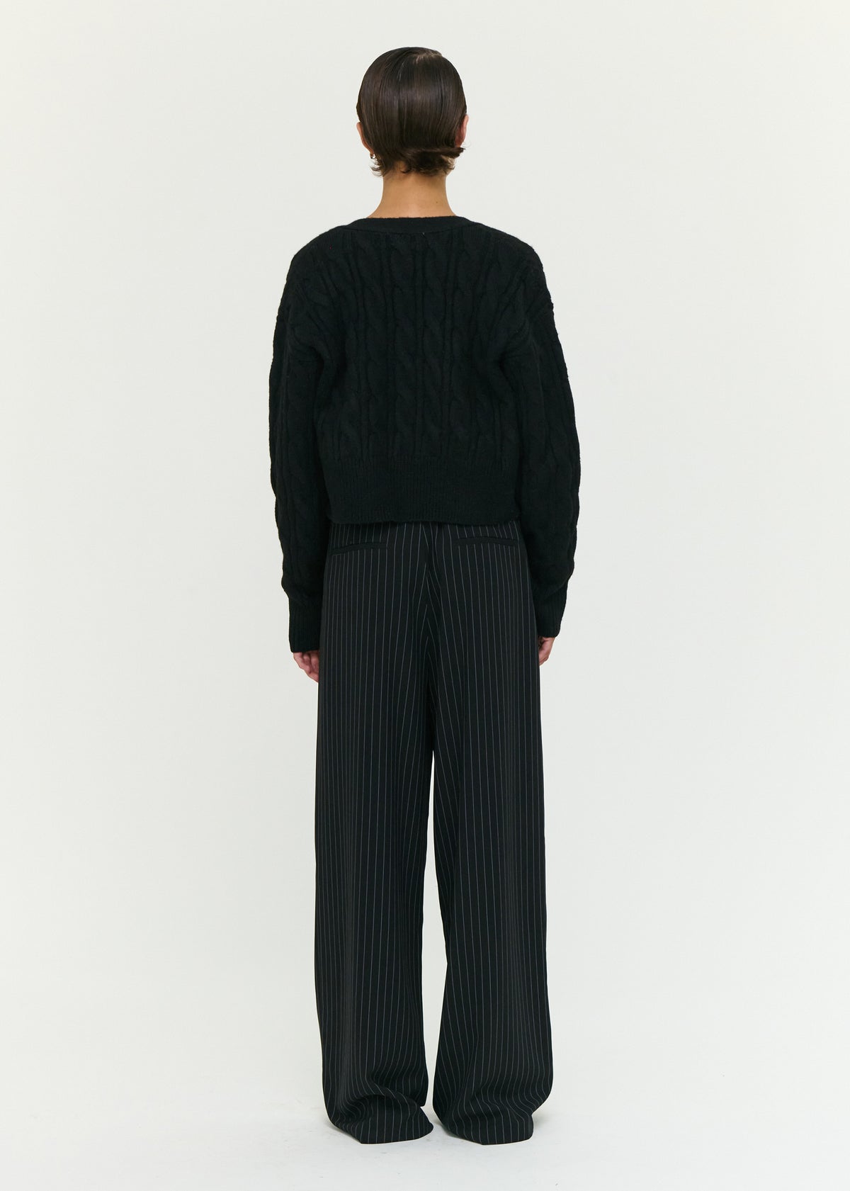 Back view of the Black Cable Knit Cropped Cardigan with a front button closure and a soft cable knit fabrication.