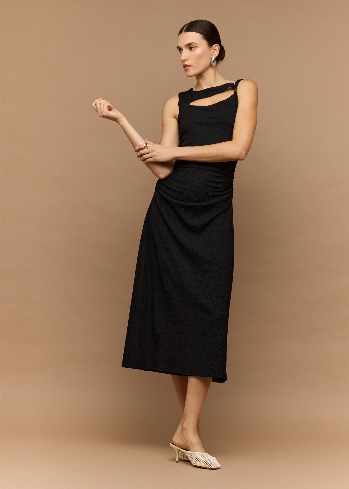 Model seated wearing Black Cut Out Ruched A-Line Midi Dress With Bead Detail with a side ruching and a sleeveless cut.