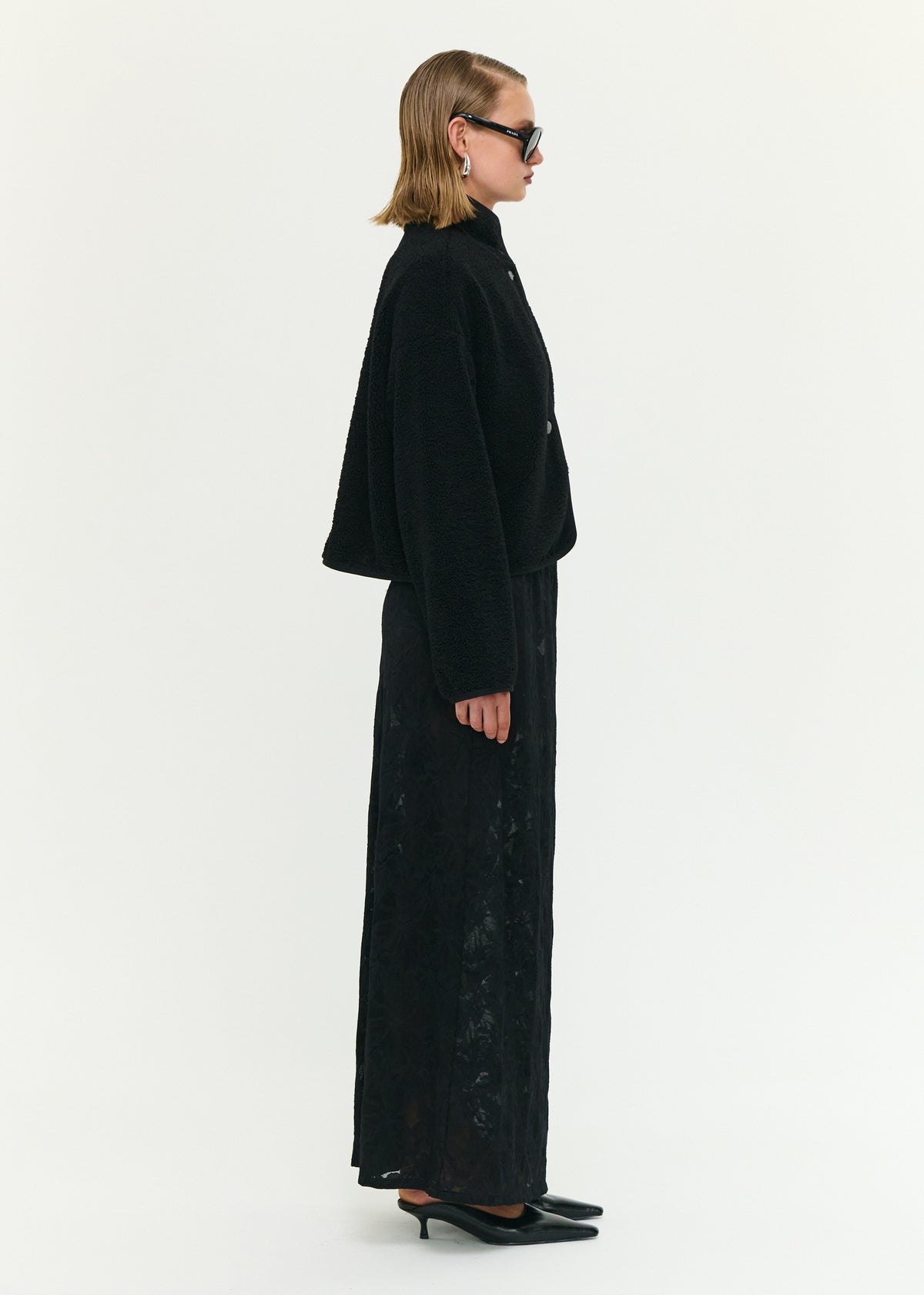 Side view of the Black High Neck Cropped Sherpa Jacket, showing a soft sherpa fabrication and a cropped silhouette.