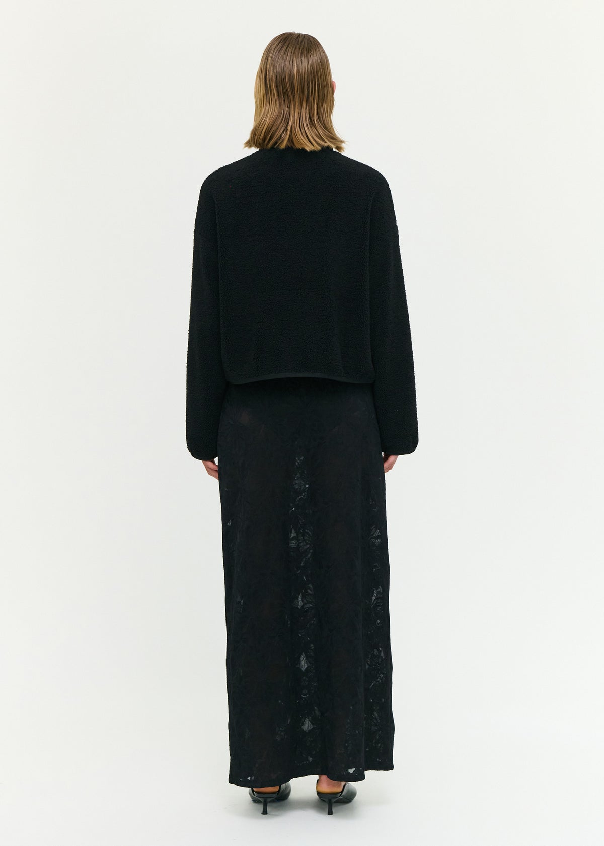 Back view of the Black High Neck Cropped Sherpa Jacket with a snap button front closure and a soft sherpa fabrication.