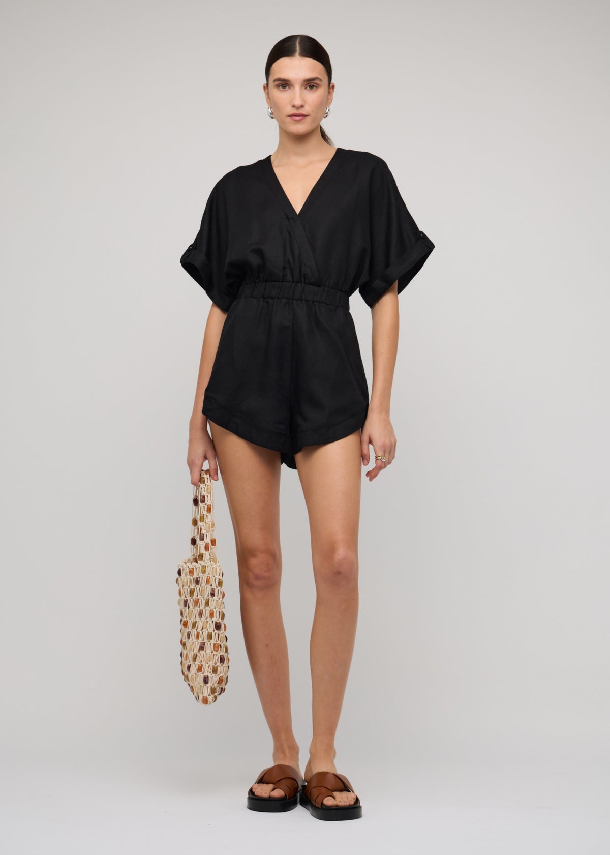Model wearing Black Linen Blend V-neck Playsuit with a v-neckline with draped front, turned to the side.
