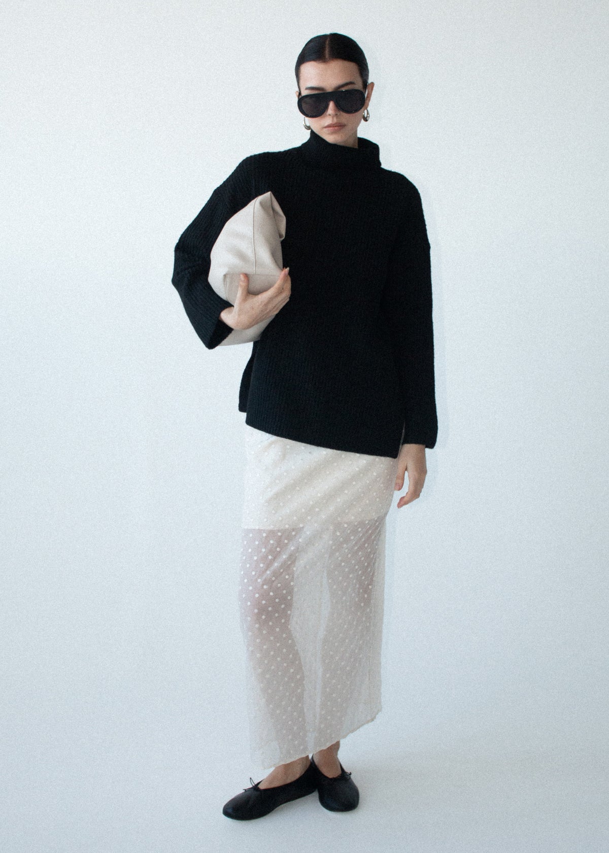 Model wearing Black Roll Neck Oversized Knit Jumper with dropped shoulder seams and a ribbed knit texture, turned to the side.