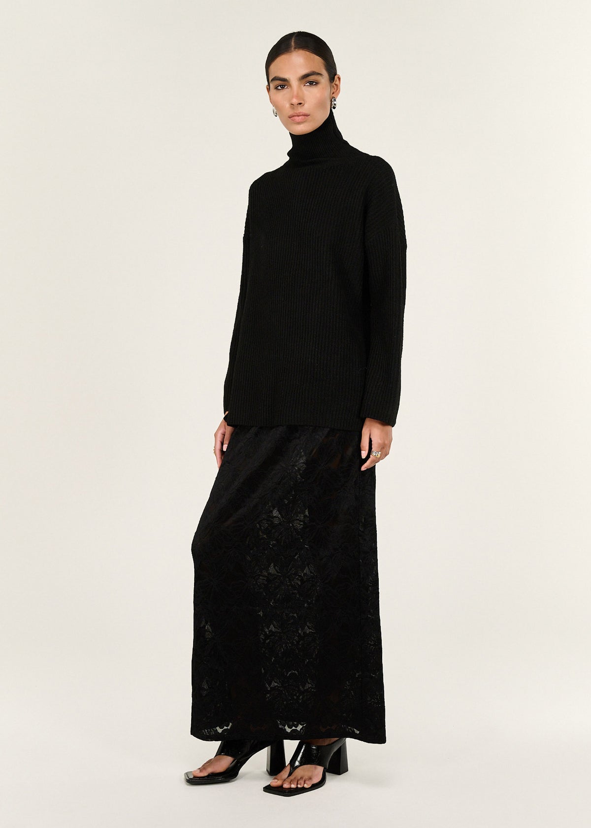 Model wearing Black Roll Neck Oversized Knit Jumper, showing dropped shoulder seams and a ribbed knit texture.