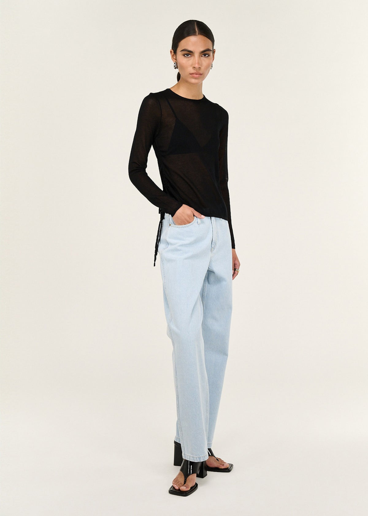 Model wearing Black Ruched Detail Sheer Knit Top with a crew neckline and long sleeves, turned to the side.