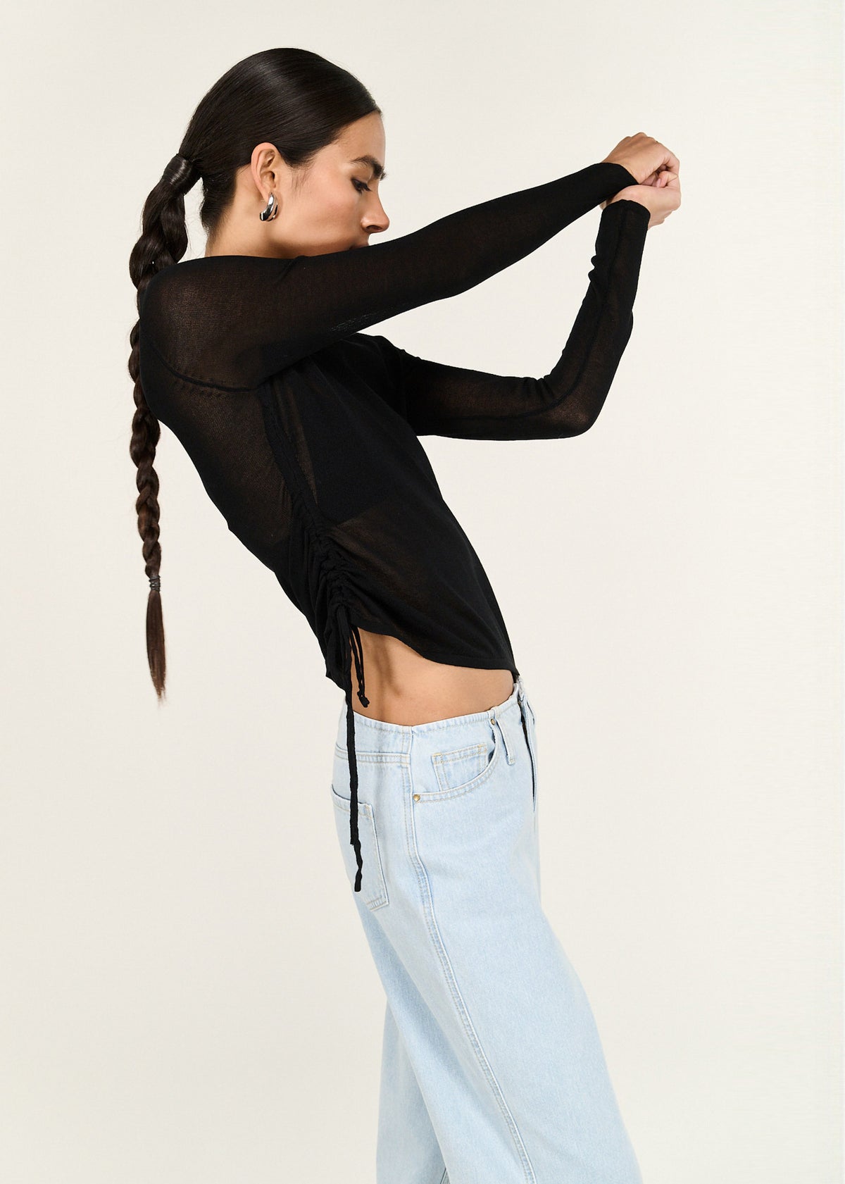 Model seated wearing Black Ruched Detail Sheer Knit Top with an adjustable drawstring side with ruched detail and a lightweight stretch.