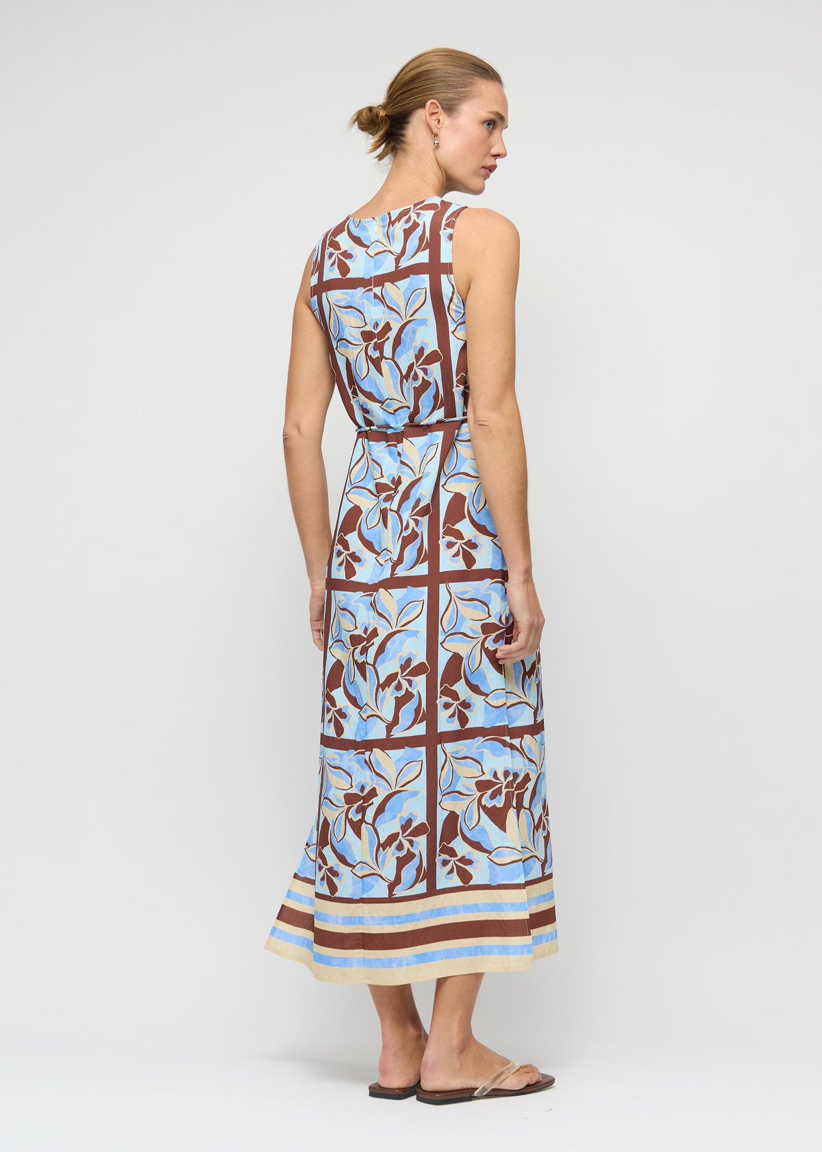 Model wearing Blue Abstract floral Midi Dress with Tie Waist with a sleeveless, high-neck silhouette and a midi length, turned to the side.