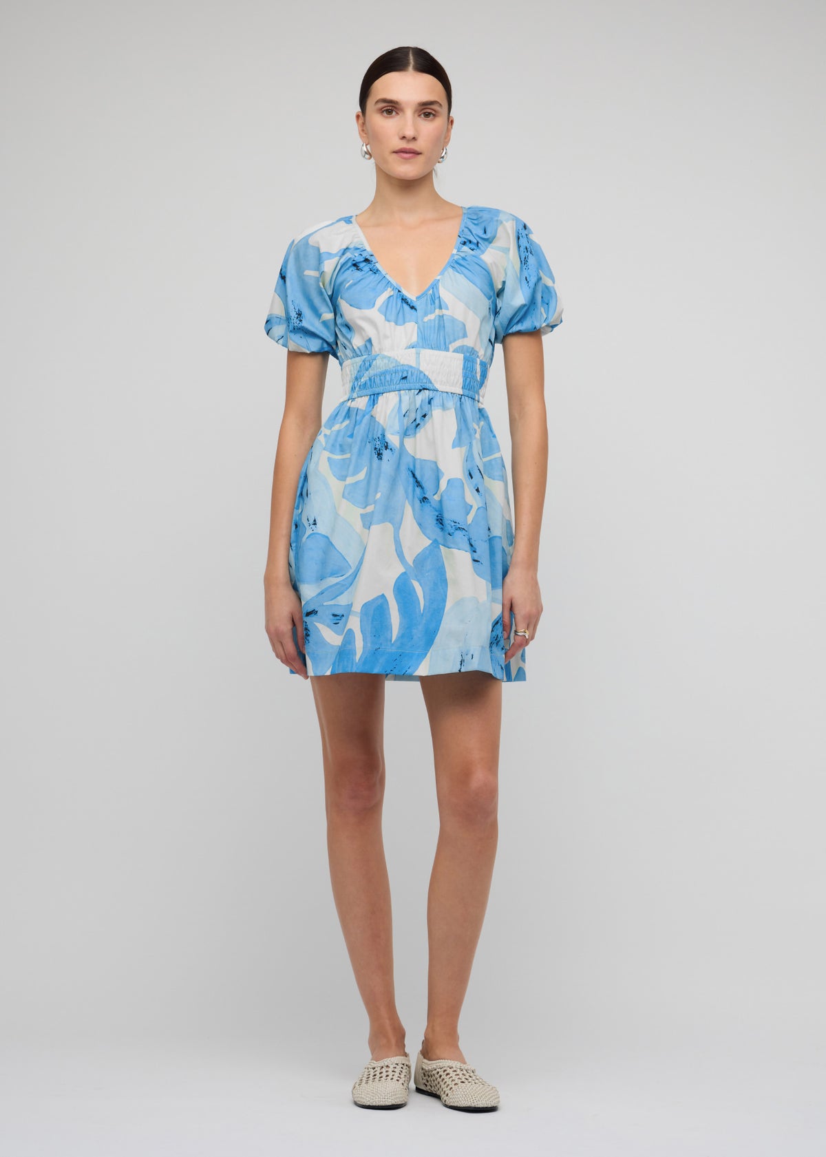 Model wearing Blue and White Floral Cotton V-Neck Mini Dress with an exclusive blue abstract Leilani print and side seam pockets.