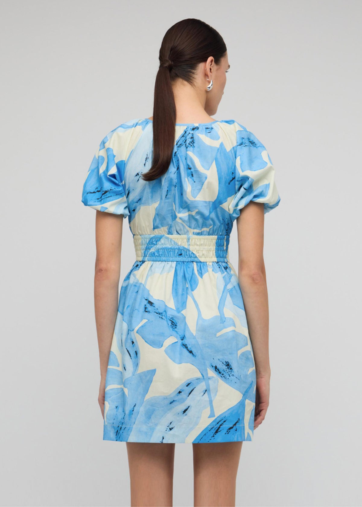 Back view of the Blue and White Floral Cotton V-Neck Mini Dress with a mini length with shirred waistband and v-neckline with puff sleeves.