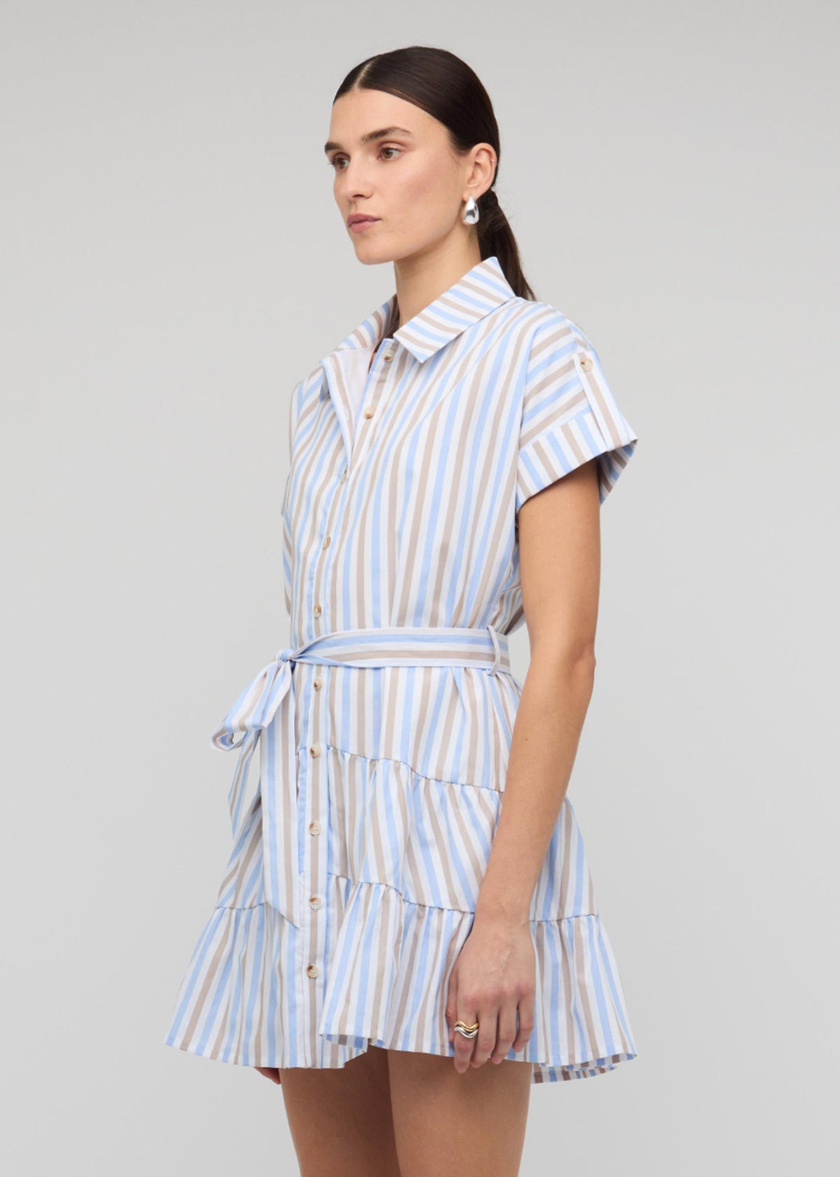 Model wearing Blue Stripe Cotton Mini Shirt Dress with a relaxed shirtdress silhouette and a button-down front, turned to the side.