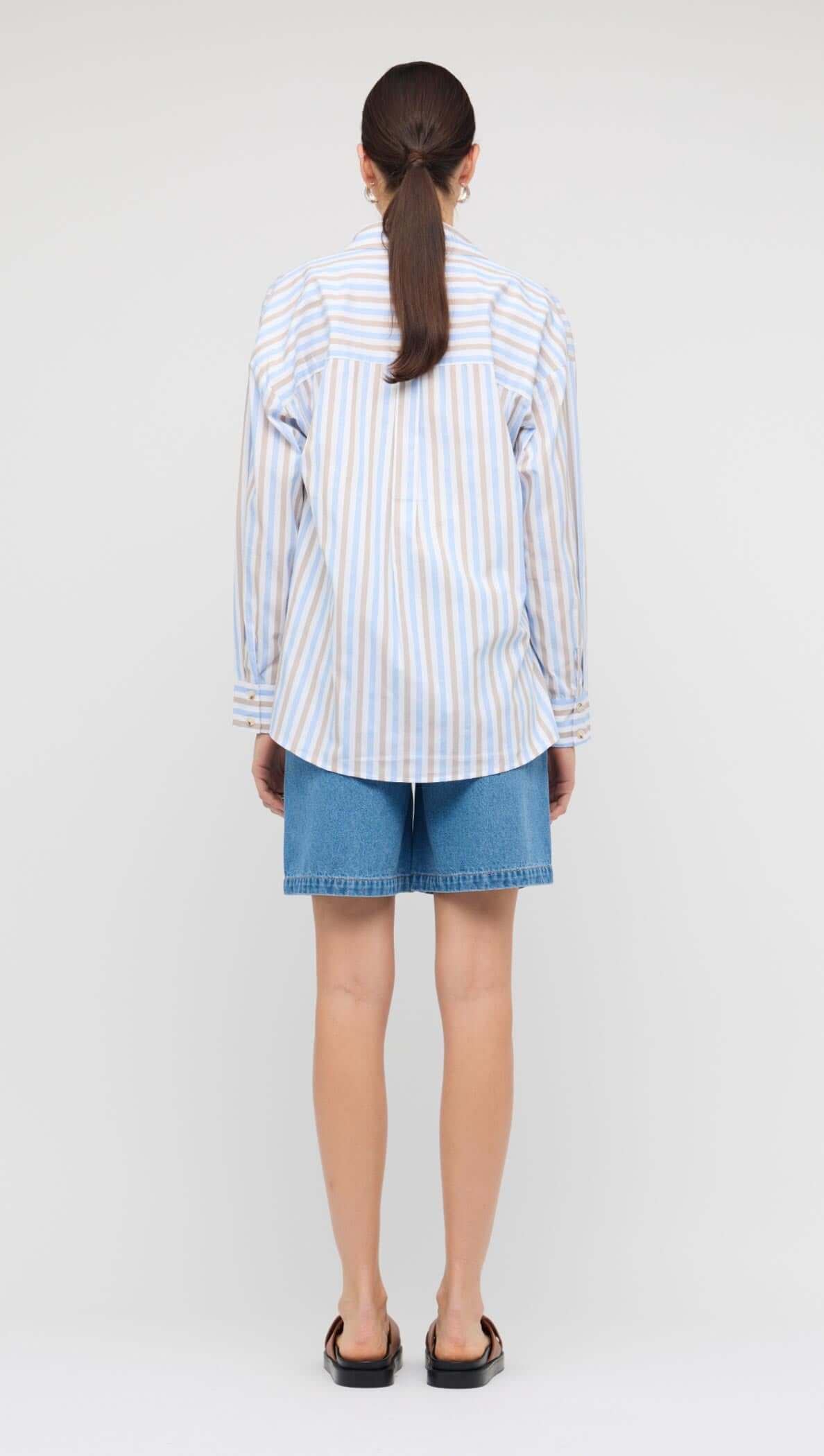 Back view of a model wearing the Blue Stripe Cotton Oversize Shirt styled with denim shorts.