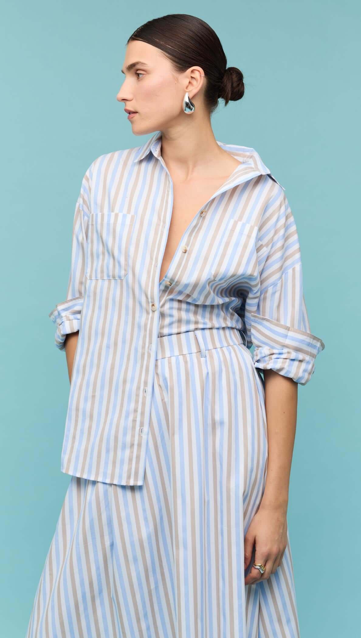 Model wearing a Blue Stripe Cotton Oversize Shirt paired with a matching skirt against a teal background.