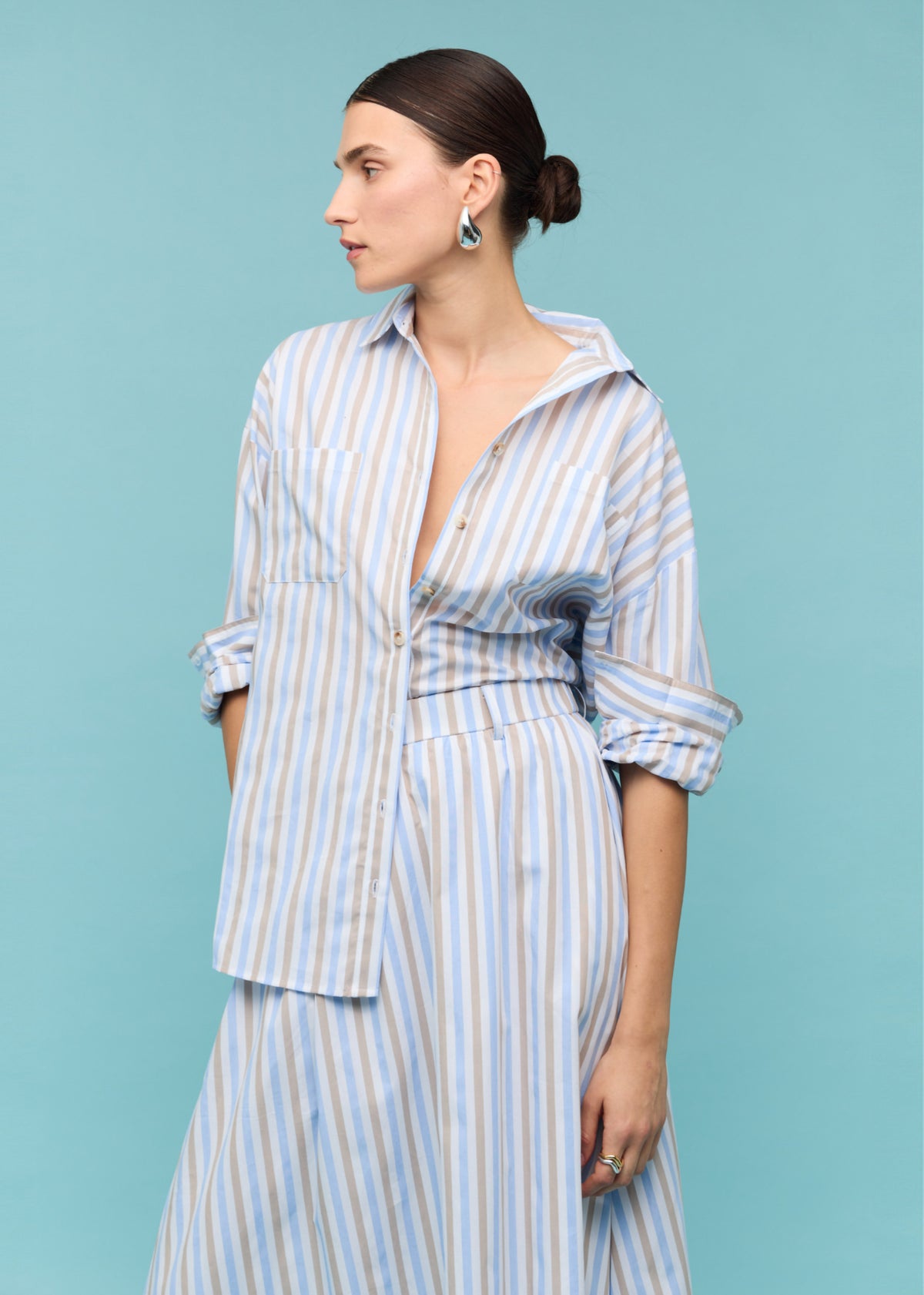 Close-up of the Blue Stripe Cotton Oversize Shirt, showing a relaxed oversized fit, photographed against a teal backdrop.