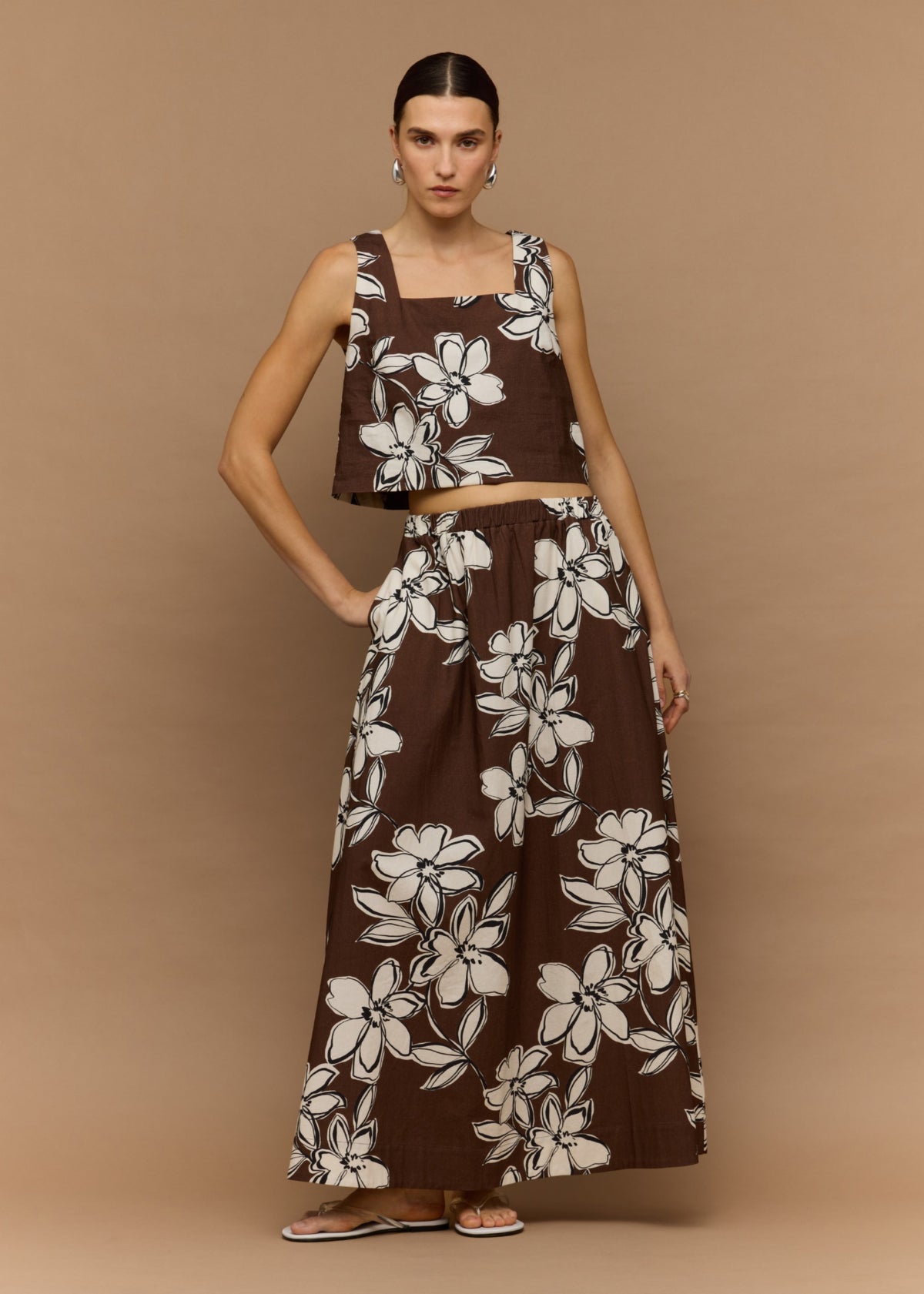 Model wearing Brown and White Cotton Floral Crop Top, showing wide straps and a cropped length, photographed against a tan studio backdrop.