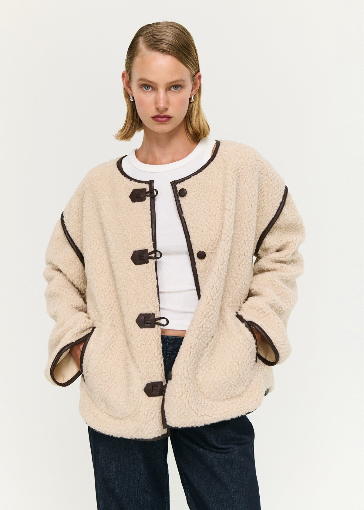 Close-up of the Brown Contrast Trim Duffle Coat in Teddy, showing a collarless neckline and long sleeves.