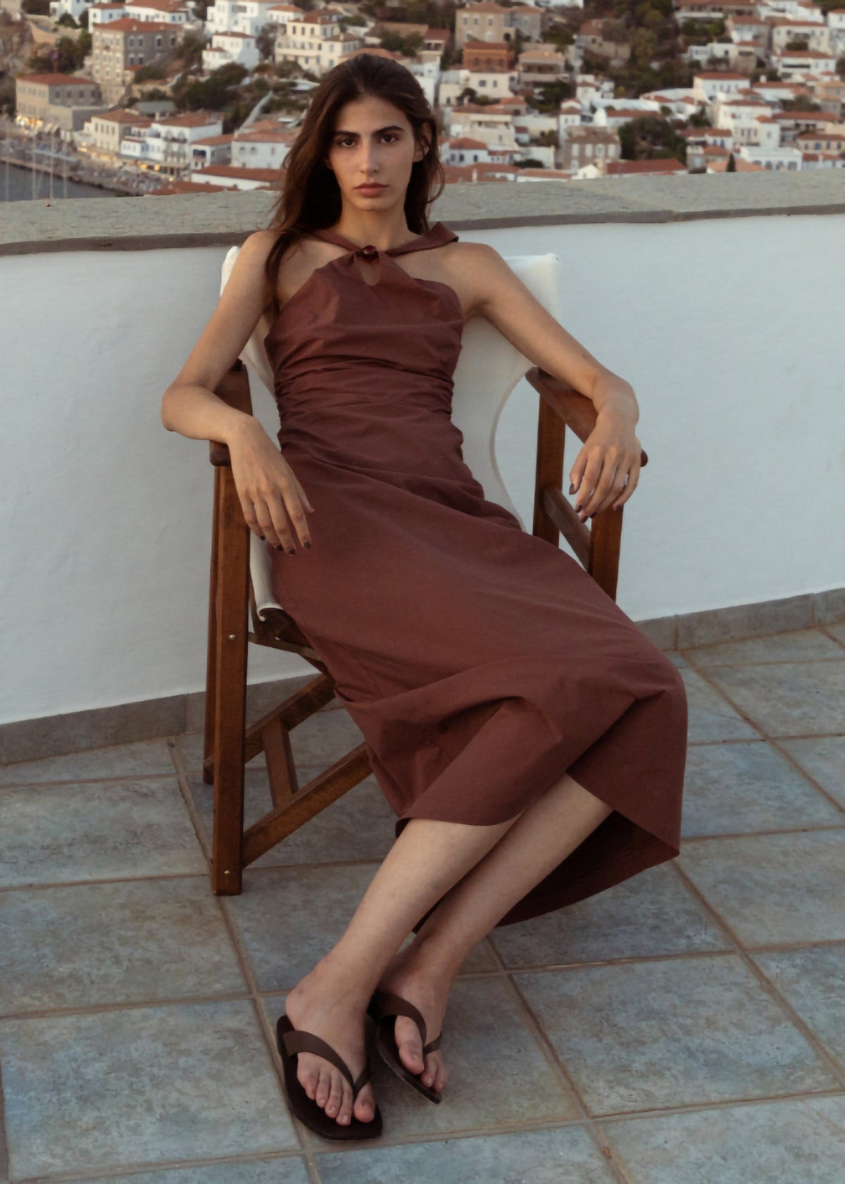 Model seated wearing Brown Cotton Bead Halter-Neck Ruched Midi Dress with a ruched bodice and a centre-back zip fastening.