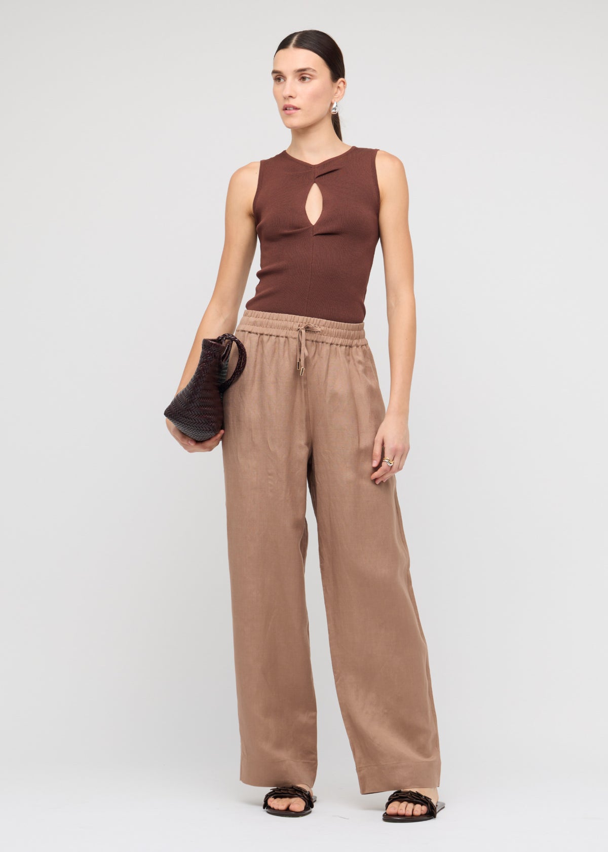 Model wearing Brown Cut-Out Sleeveless Knit Top with a sleeveless cut and a ribbed stretch fabrication, turned to the side.