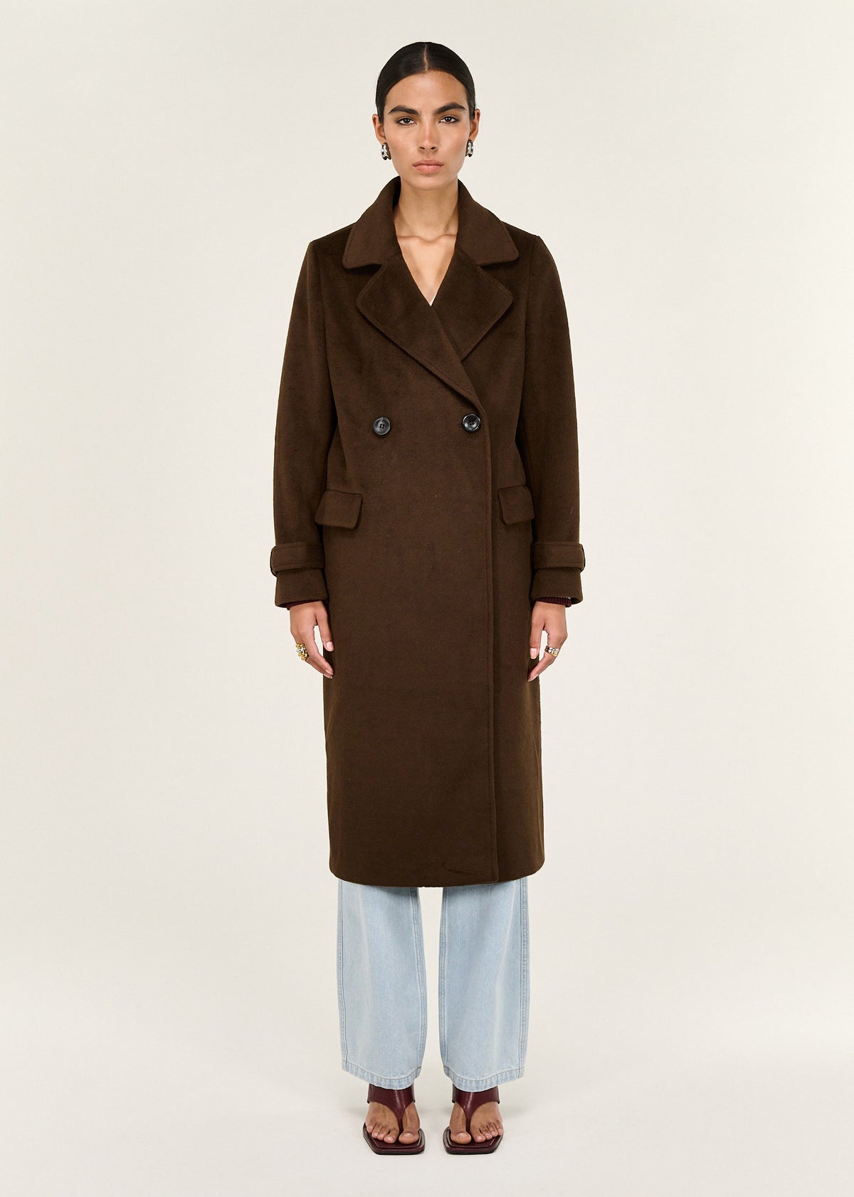Model wearing Brown Double-Breasted Longline Coat, showing functional front flap pockets and a back vent.