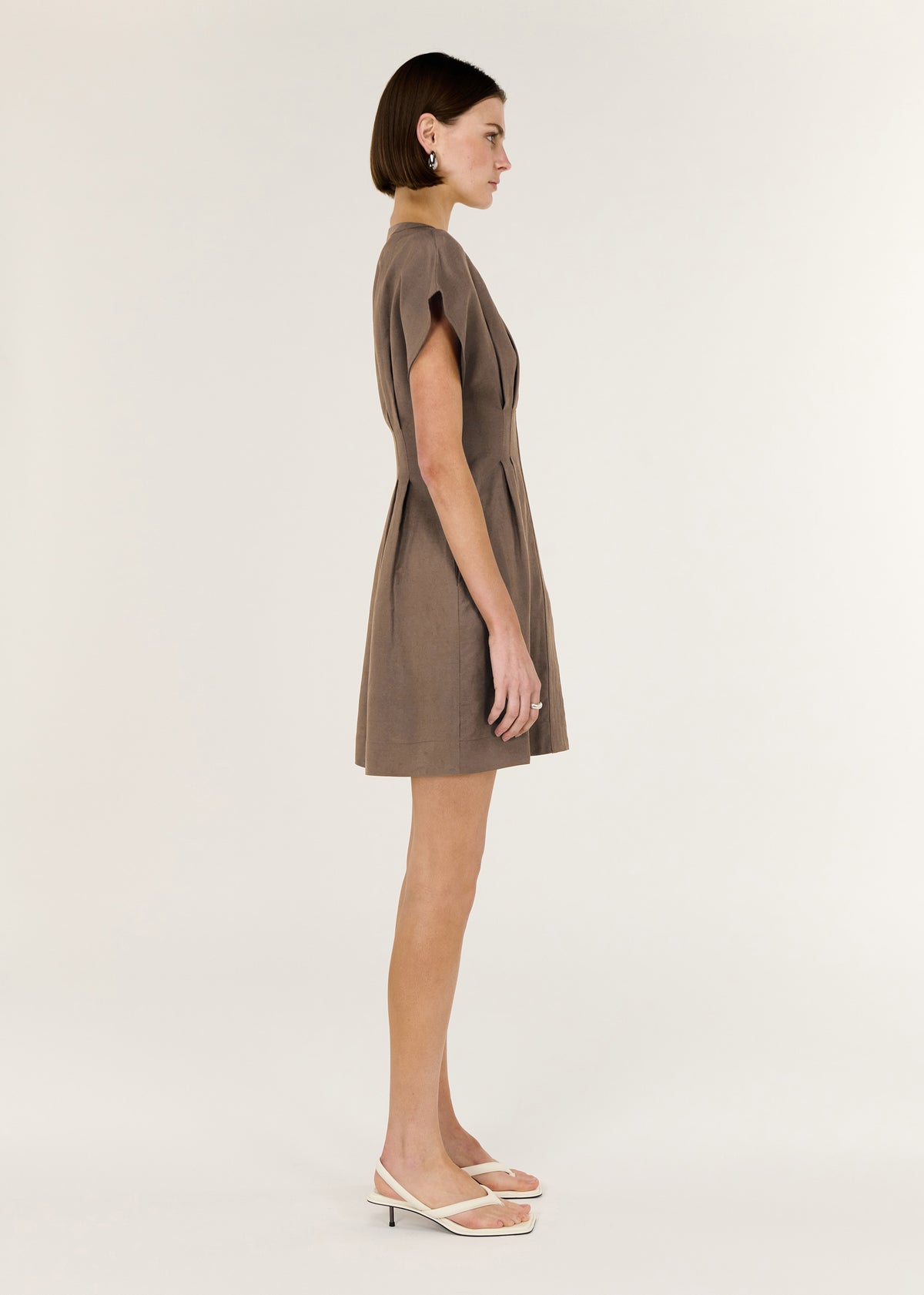 Side view of the Brown Linen Blend Pleated Mini Dress, showing a tailored silhouette with panel detailing and soft cap sleeves.