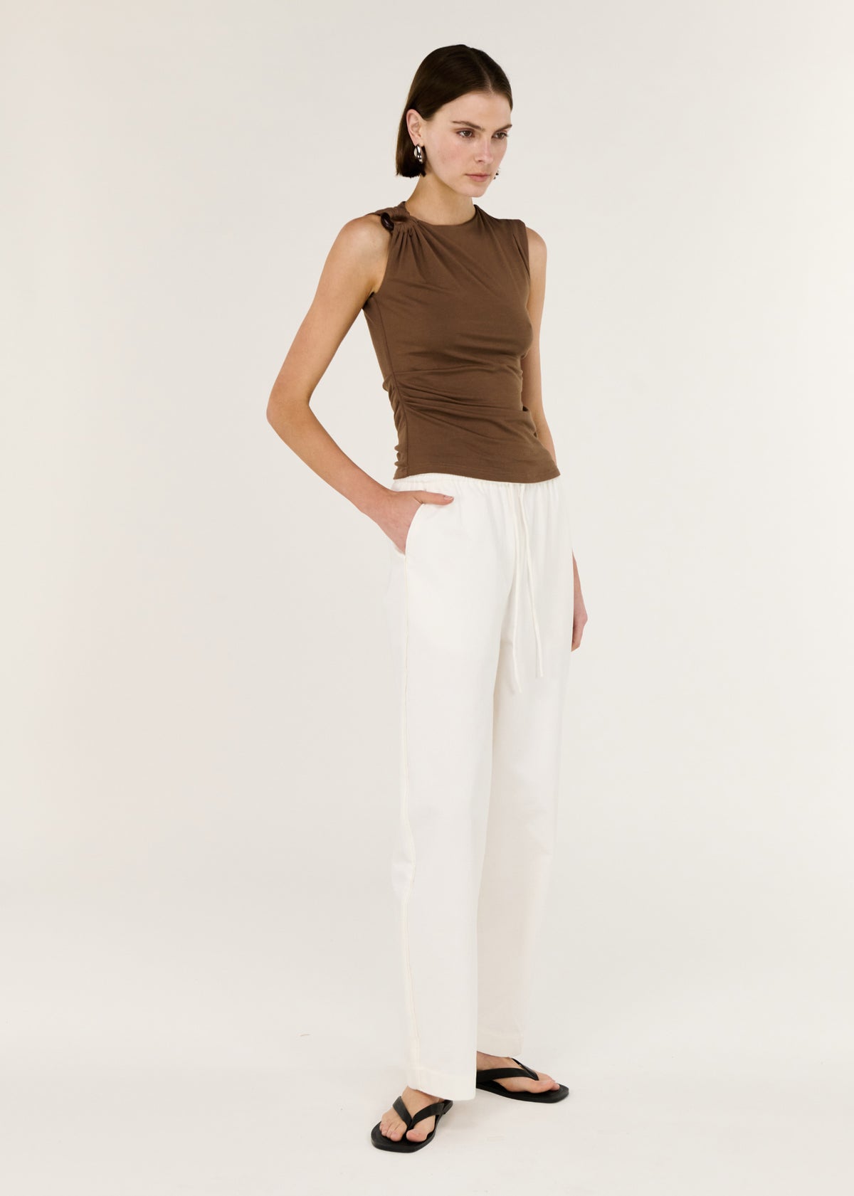 Model wearing Brown Ruched Slinky Tank with a stretch fabrication and a sleeveless cut.