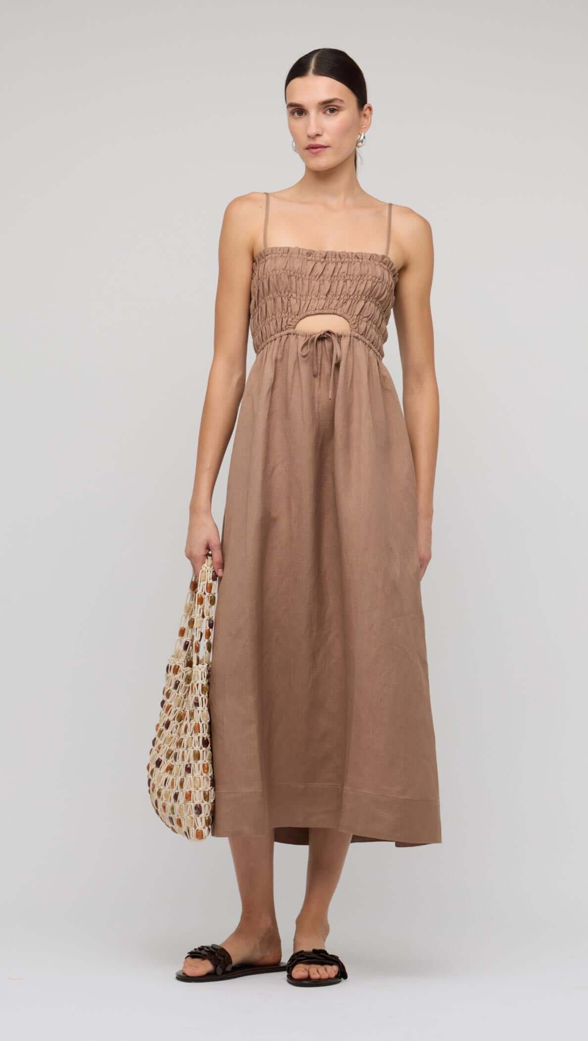 Brown Shirred Cut-Out Linen Midi Dress worn by model with a bag in a neutral background.