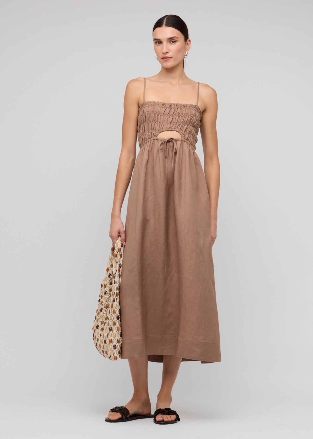 Model wearing Brown Shirred Cut-Out Linen Midi Dress with a shirred fitted bodice with tie-front detail and a subtle cut-out at the waist.