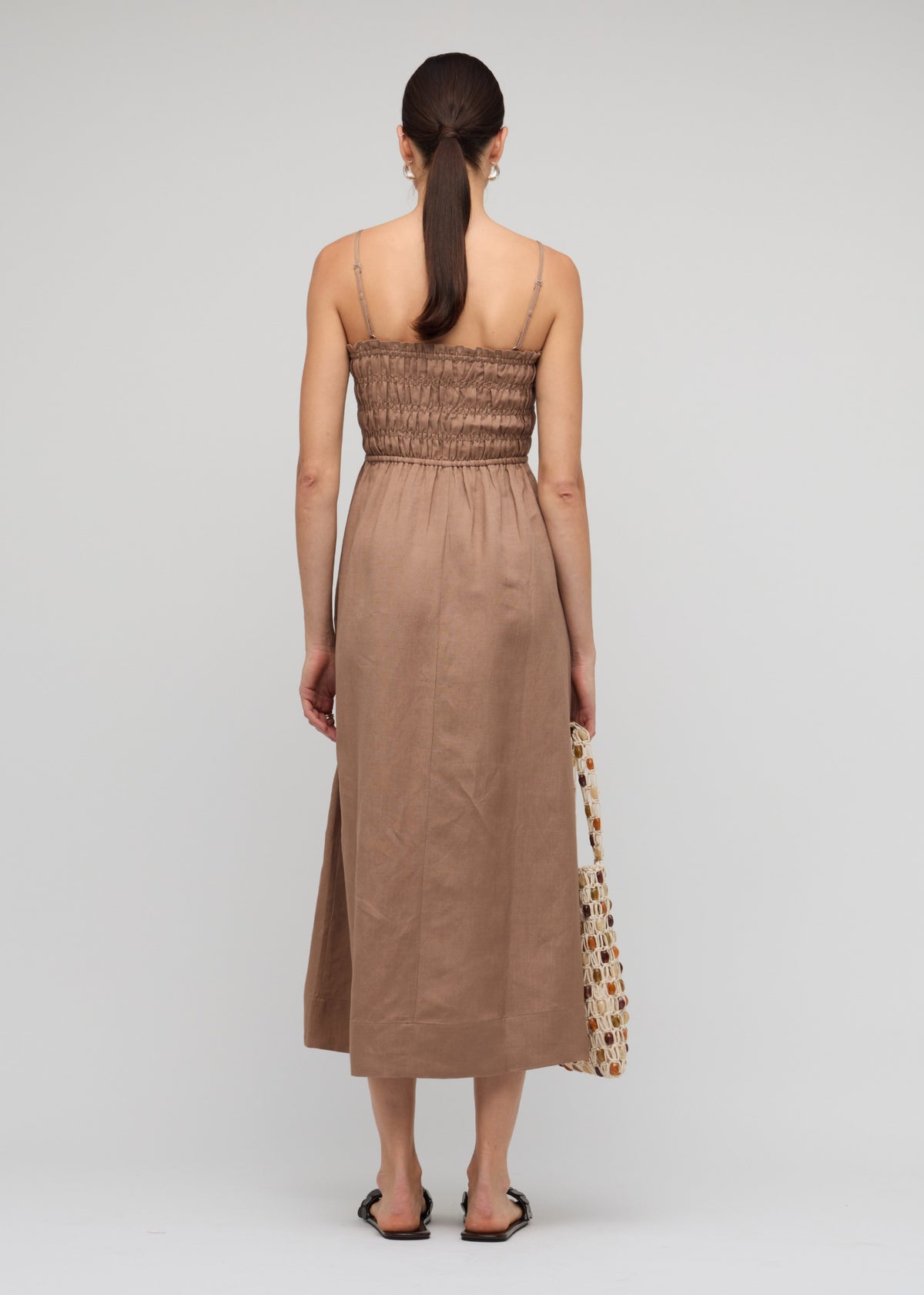 Back view of the Brown Shirred Cut-Out Linen Midi Dress with a shirred fitted bodice with tie-front detail and adjustable spaghetti straps.