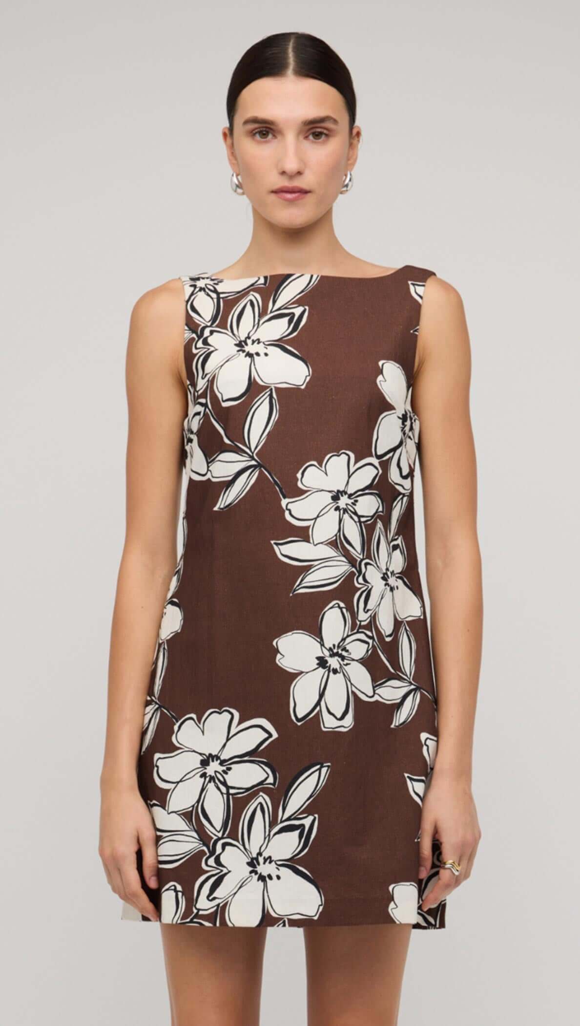 Model wearing a brown and white floral shift mini dress, holding a black bag, showcasing a stylish summer look.