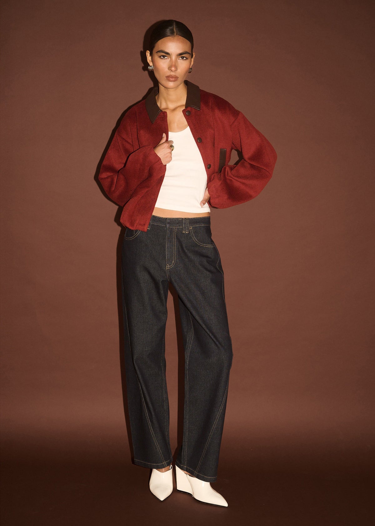 Model wearing Burgundy Brushed Bomber Jacket with a soft textured fabrication, photographed against a brown studio backdrop.