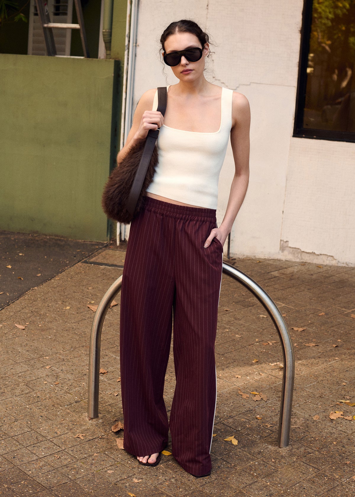 Model wearing Burgundy Pinstripe Relaxed Pant, showing a relaxed straight-leg silhouette and a mid-rise fit, photographed at a city street.