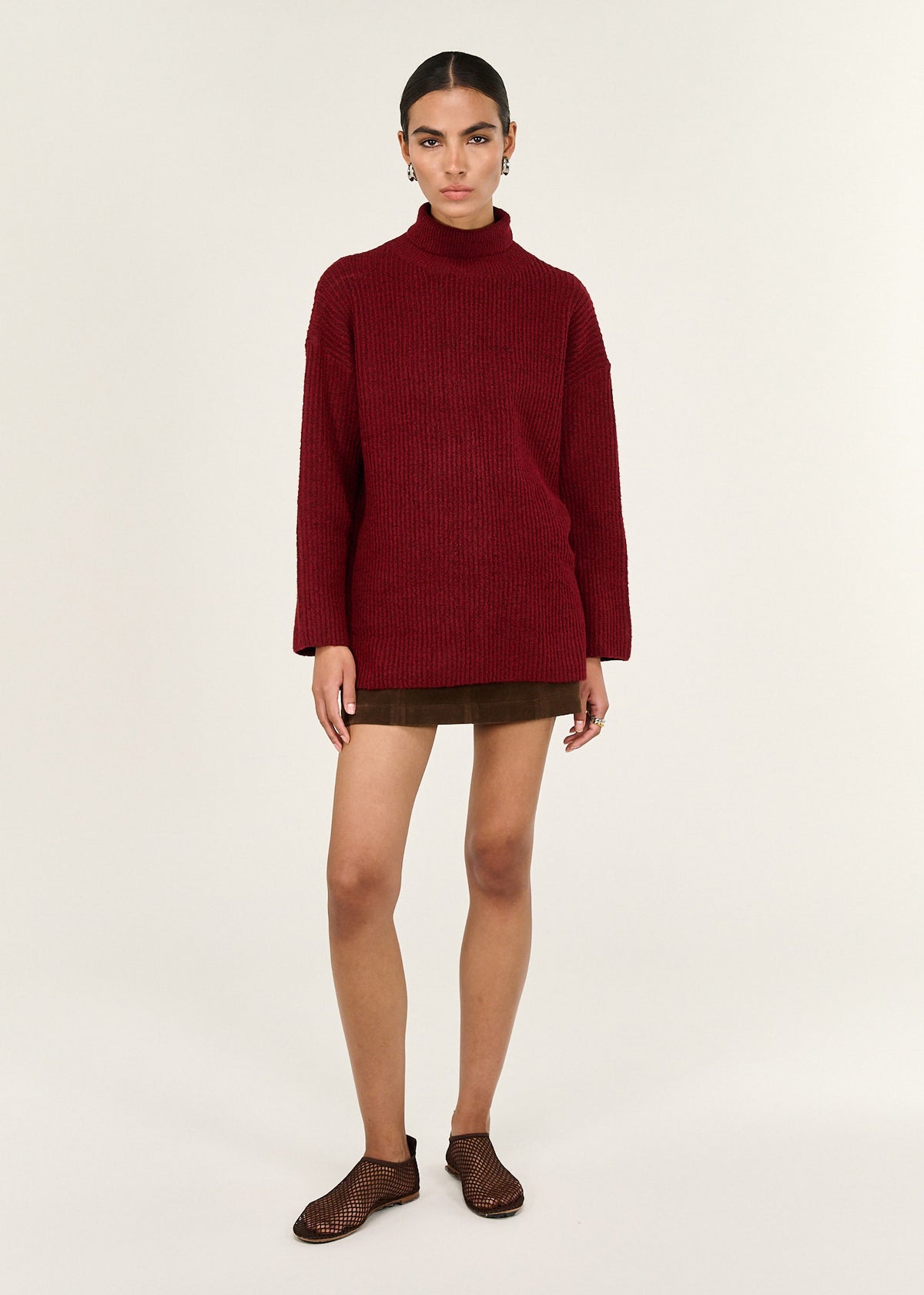 Model wearing Burgundy Roll Neck Oversized Knit Jumper, showing dropped shoulder seams and a ribbed knit texture.