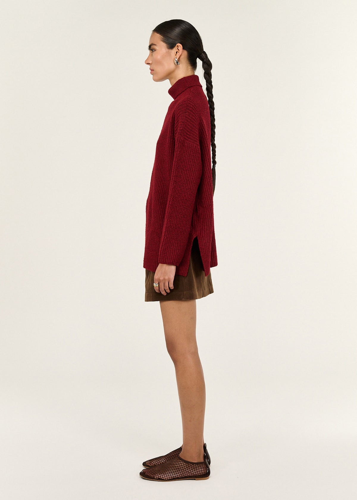 Model wearing Burgundy Roll Neck Oversized Knit Jumper with side hem splits and long sleeves, turned to the side.