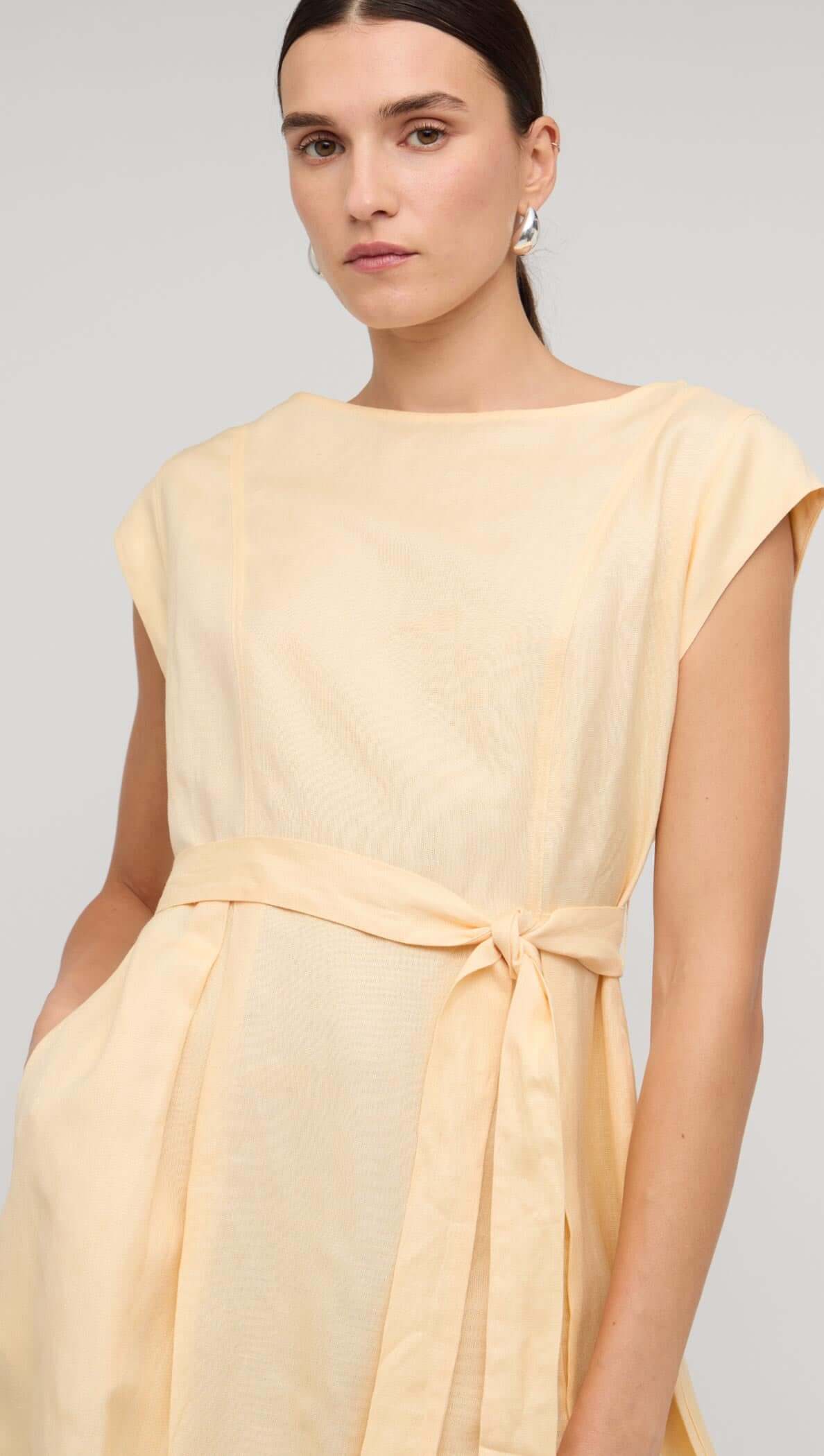 Model wearing a Butter Yellow Linen Mini Dress with cap sleeves and a self-tie belt.