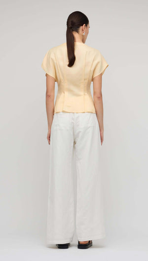 Back view of the Butter Yellow Linen Pleated Blouse styled with flowy white pants.