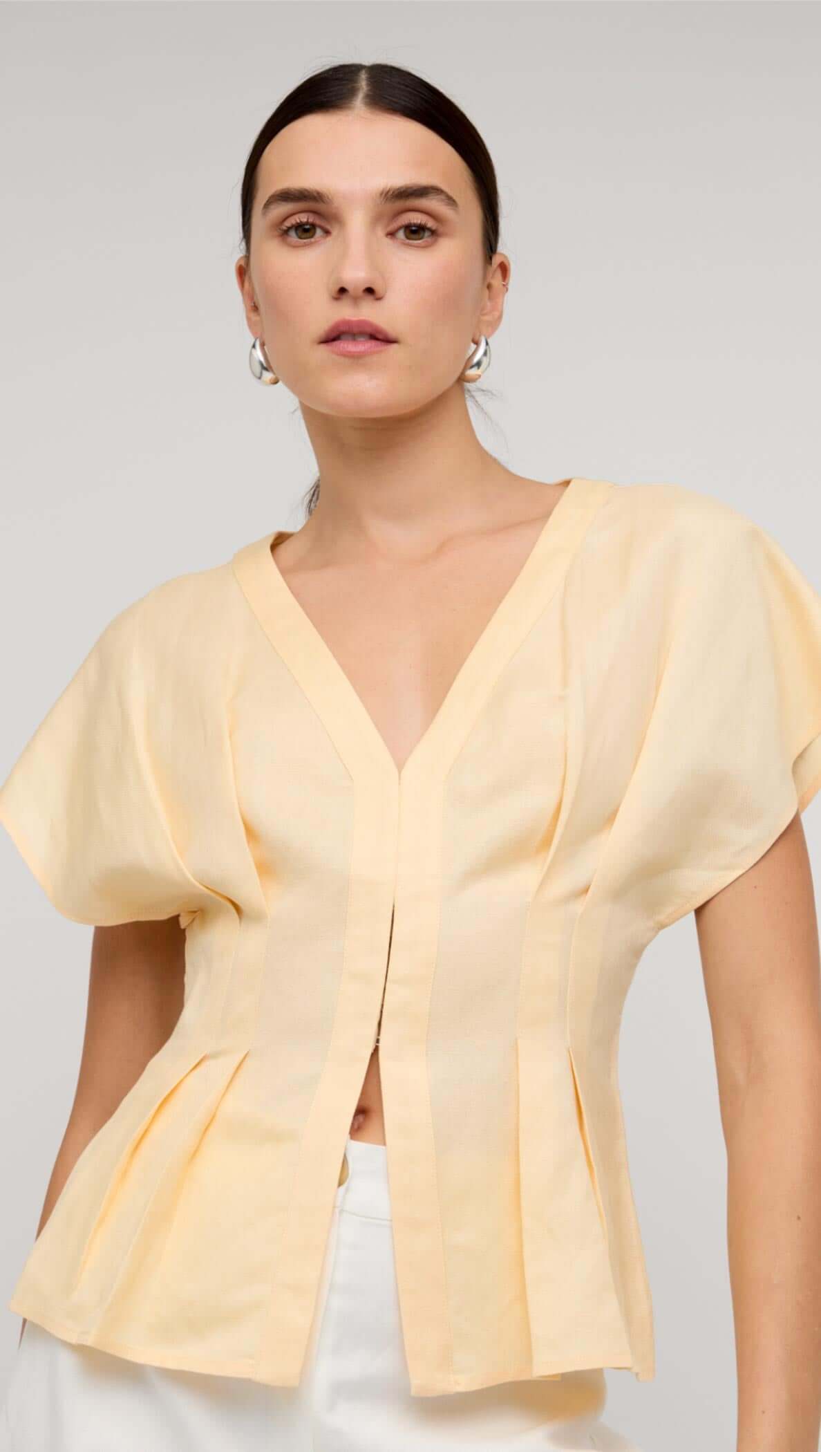 Butter Yellow Linen Pleated Blouse worn by a model showcasing its deep V-neckline and sculpted pleats.