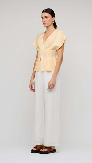 Butter Yellow Linen Pleated Blouse worn with white wide-leg pants and sandals, showcasing elegant design and flattering silhouette.
