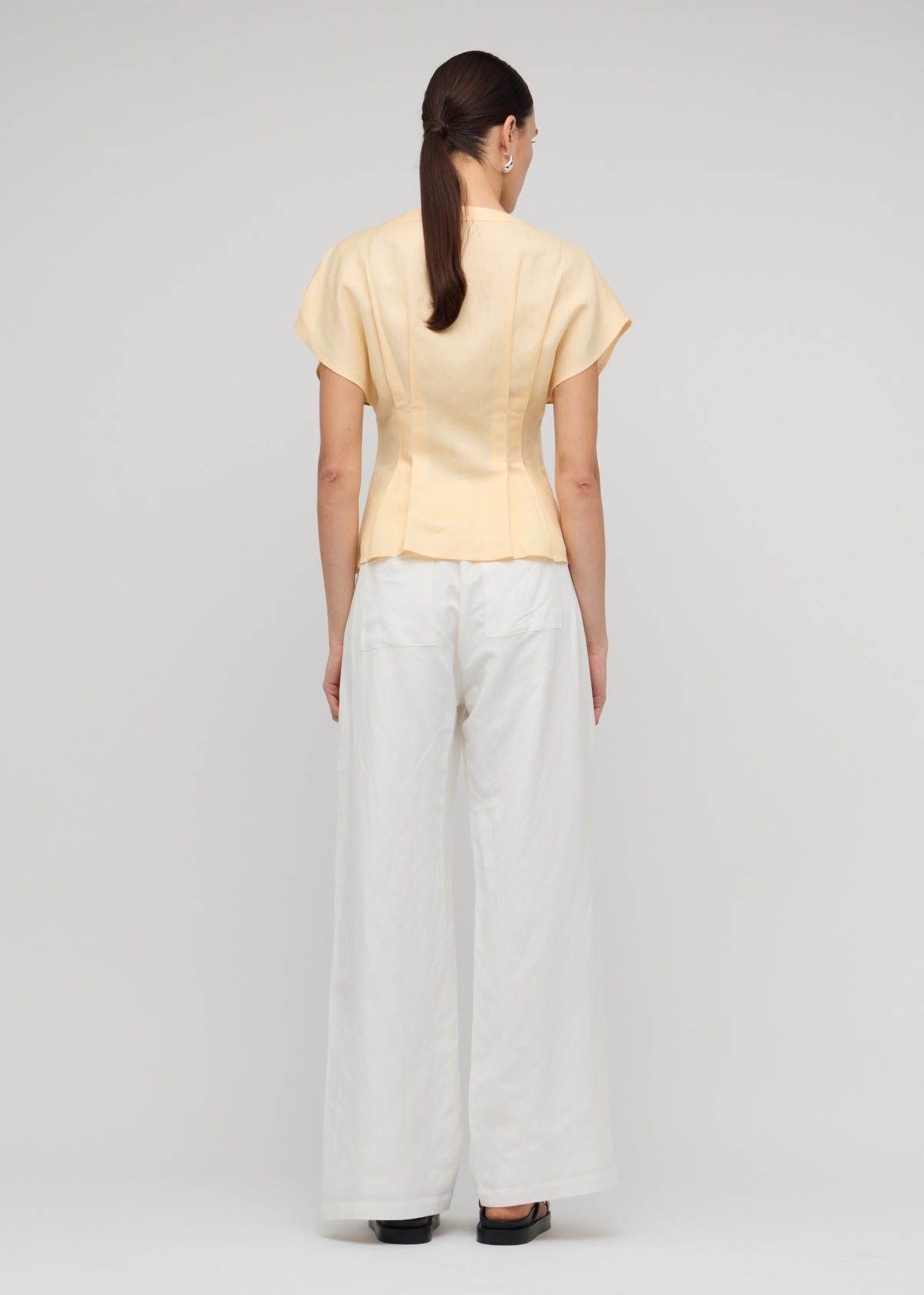 Back view of the Butter Yellow Linen Pleated Blouse with a soft butter yellow shade and a deep V-neckline.