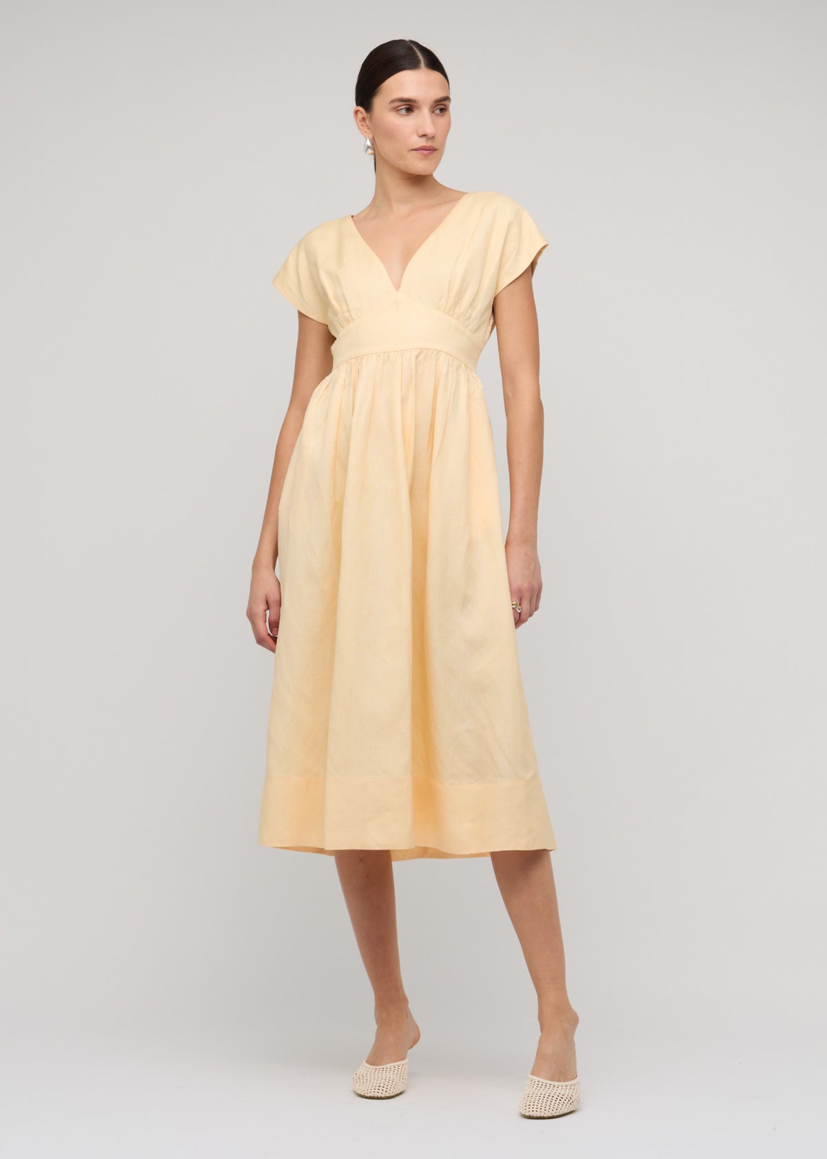 Model wearing Butter Yellow Linen V-Neck Midi Dress with a soft pastel yellow tone and deep V-neckline with cap sleeves.