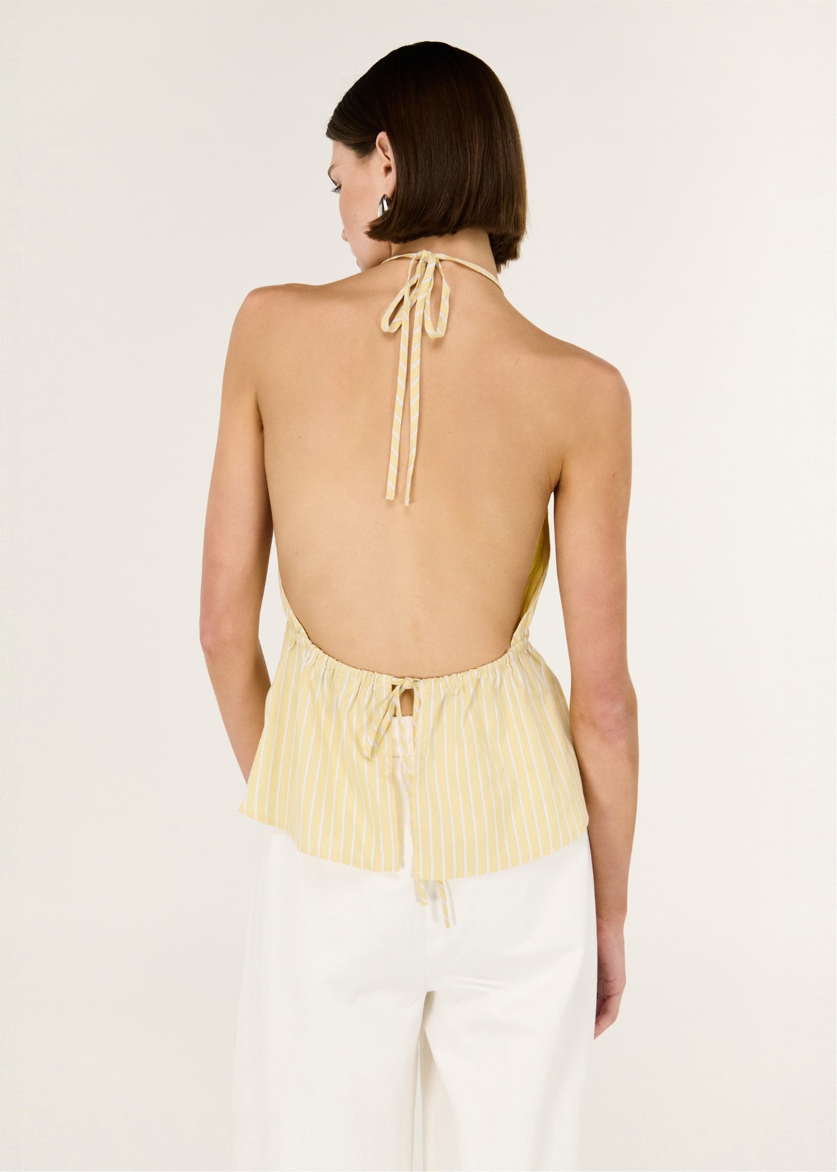 Back view of the Butter Yellow Low Back Striped Halter Top with a halter neckline with adjustable tie and an open back design.