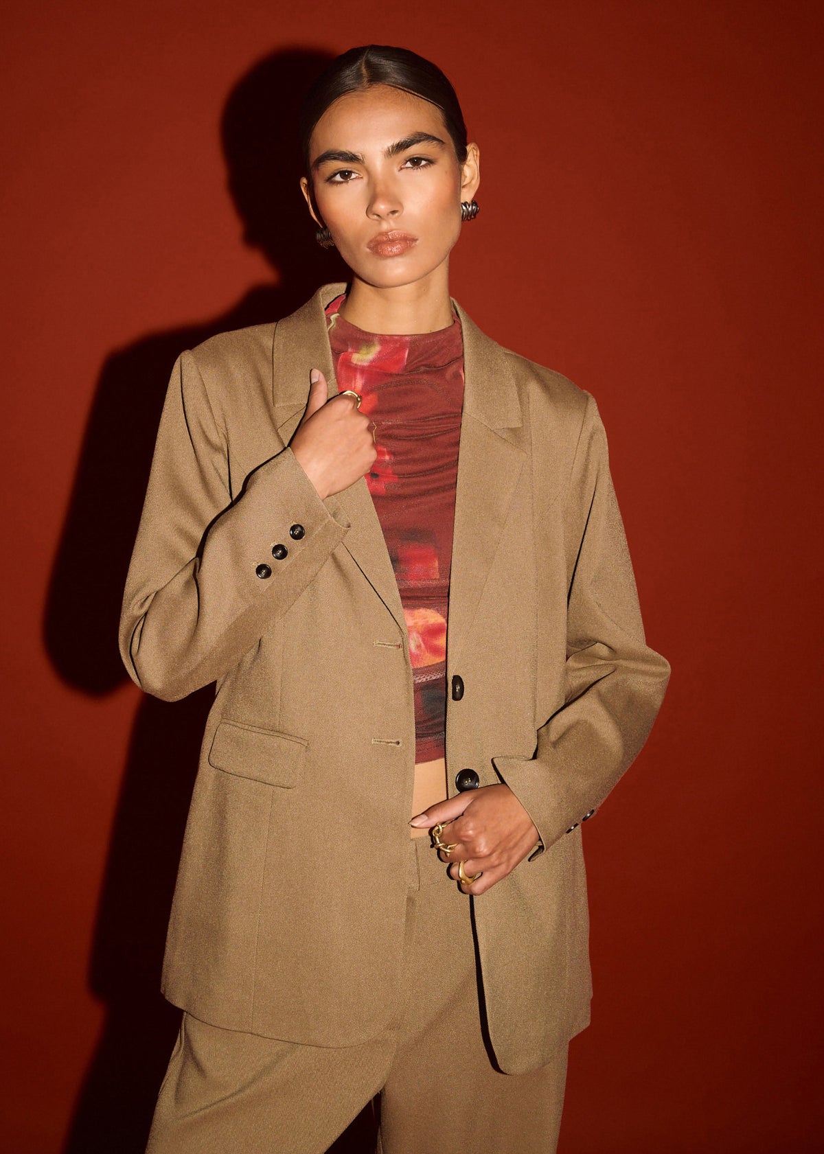 Close-up of the Chai Relaxed Tailored Blazer, showing a button cuff detailing and a relaxed fit, photographed against a red studio backdrop.