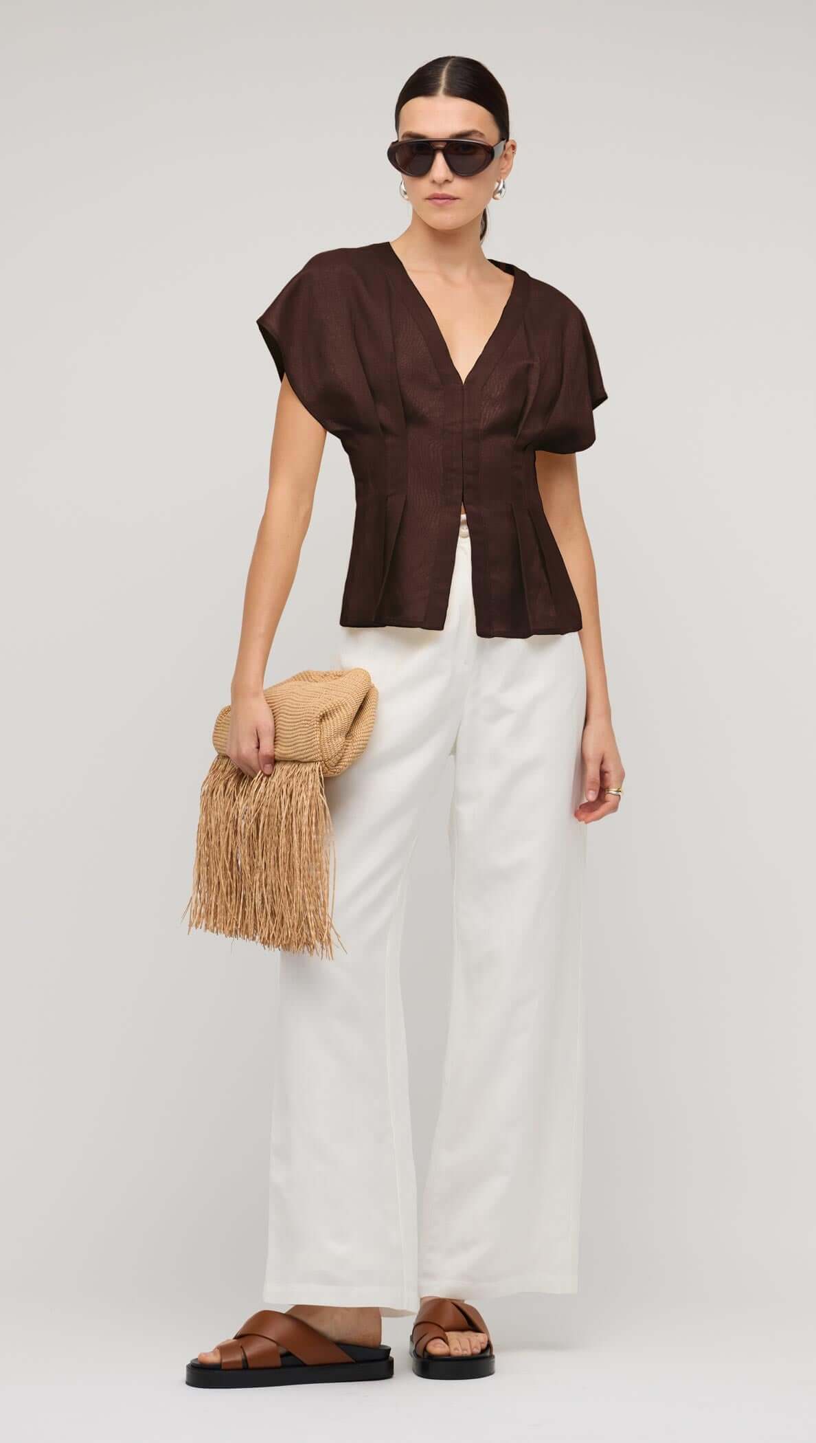 Woman modeling a chocolate brown linen pleated V-neck blouse with structured sleeves.