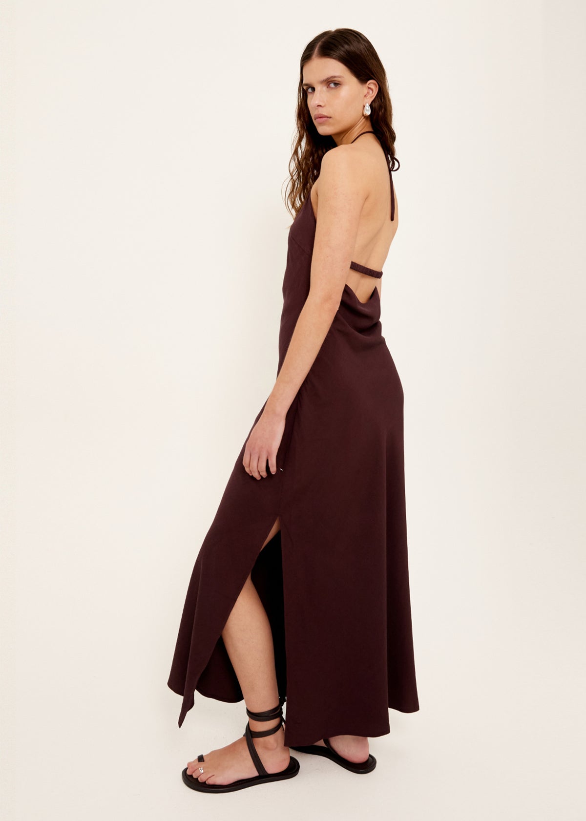 Angled view of the Chocolate Halter Midi Dress with an open back with strap detail and a side split at hem.