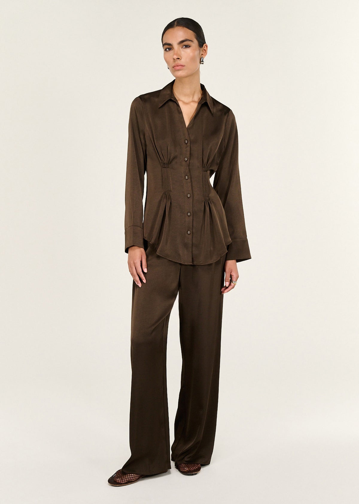 Model wearing Chocolate Pintuck Cinched Waist Satin Shirt with a classic collar and a long sleeves with cuff detail.