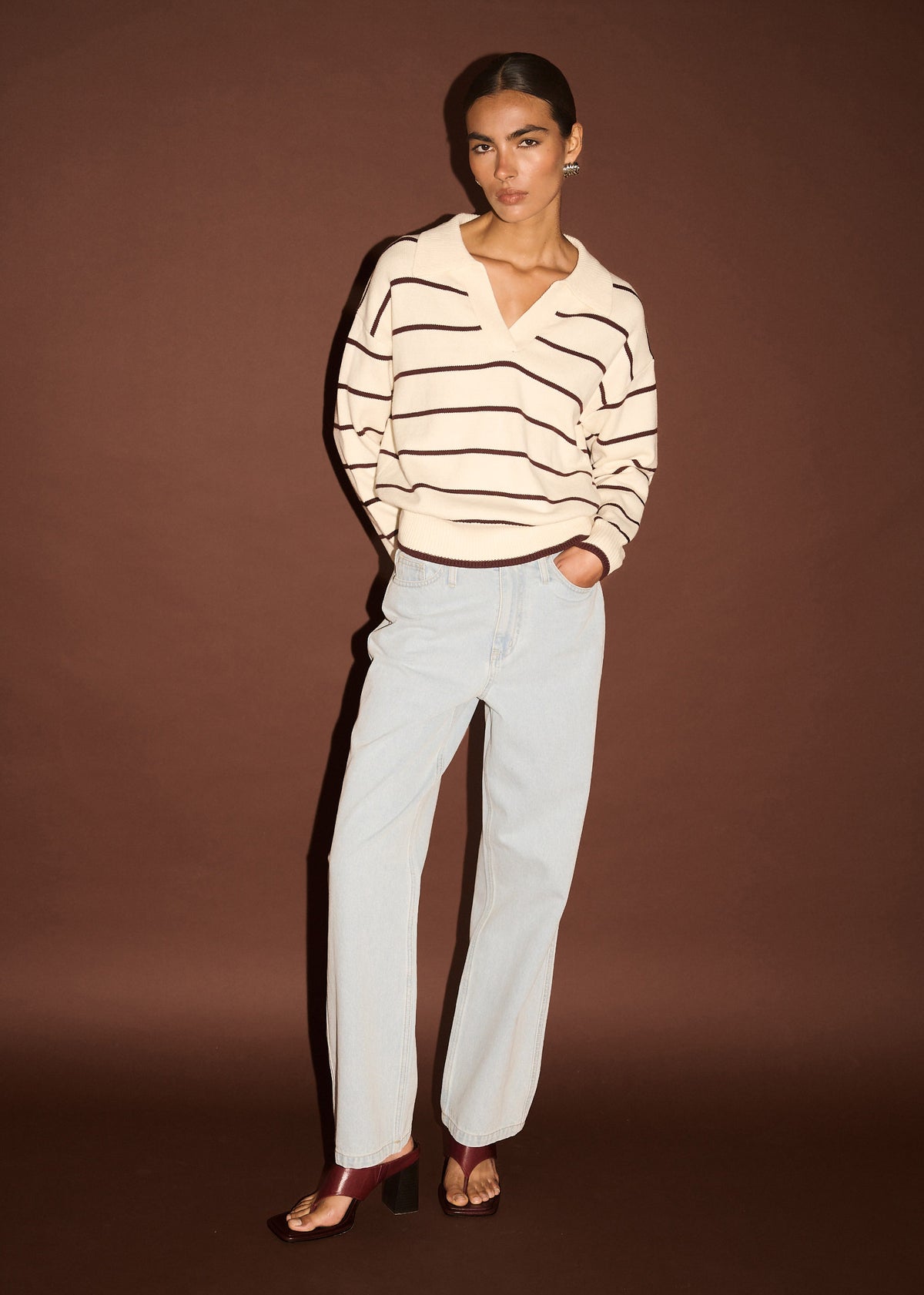 Model wearing Chocolate Stripe Polo Knit Jumper with a relaxed fit and dropped shoulders, photographed against a brown backdrop.