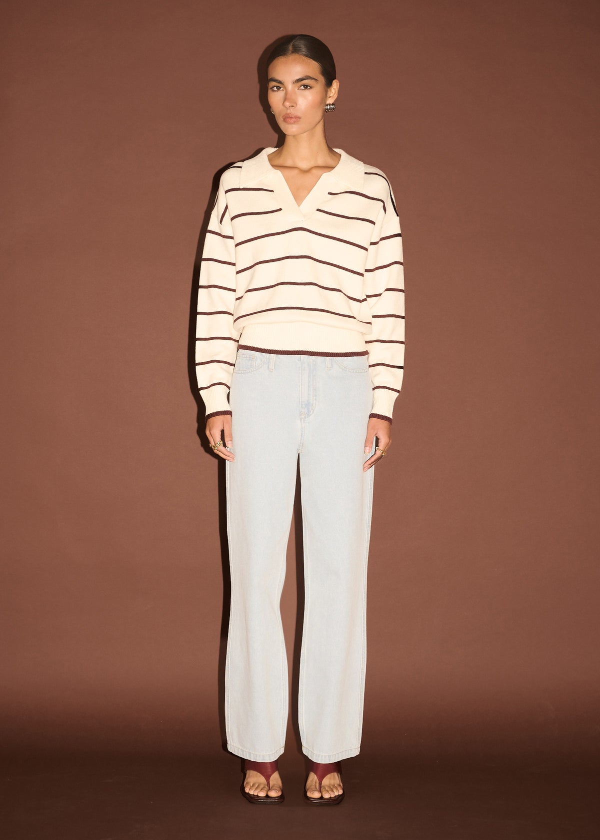Model wearing Chocolate Stripe Polo Knit Jumper, showing long sleeves, photographed against a brown backdrop.