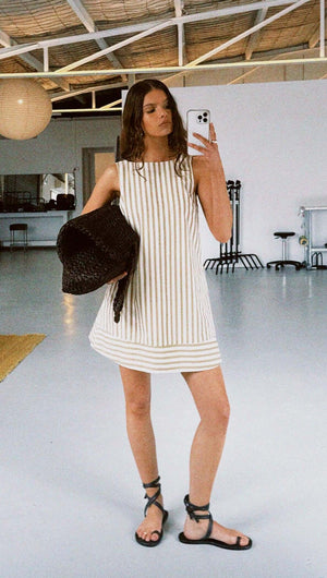 Model wearing a Cotton Stripe Mini Shirt Dress with a relaxed fit and low back, paired with a straw bag.