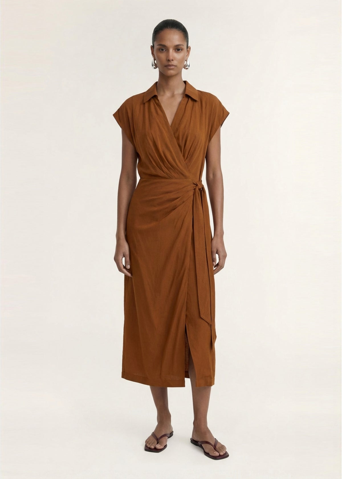 Model wearing Copper Draped Wrap Midi Dress with a fluid woven fabrication and an open collar neckline.