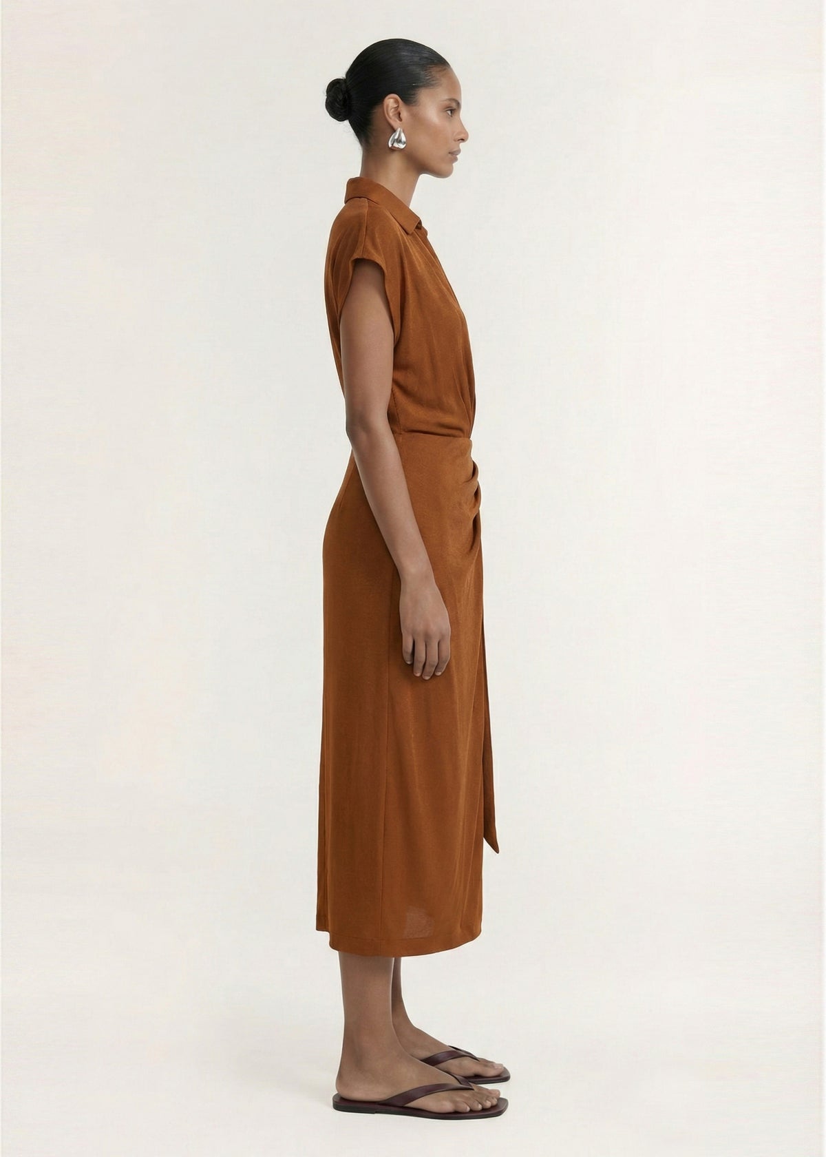 Side profile of the Copper Draped Wrap Midi Dress with a gathered waist detailing and a front split.