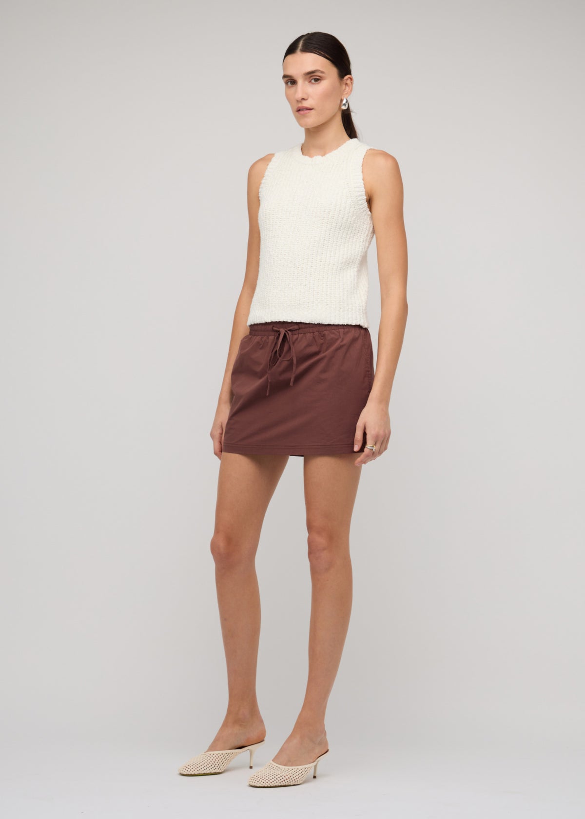 Model wearing Cotton-Blend Knit Tank Top In White with a sleeveless cut and a crew neckline, turned to the side.