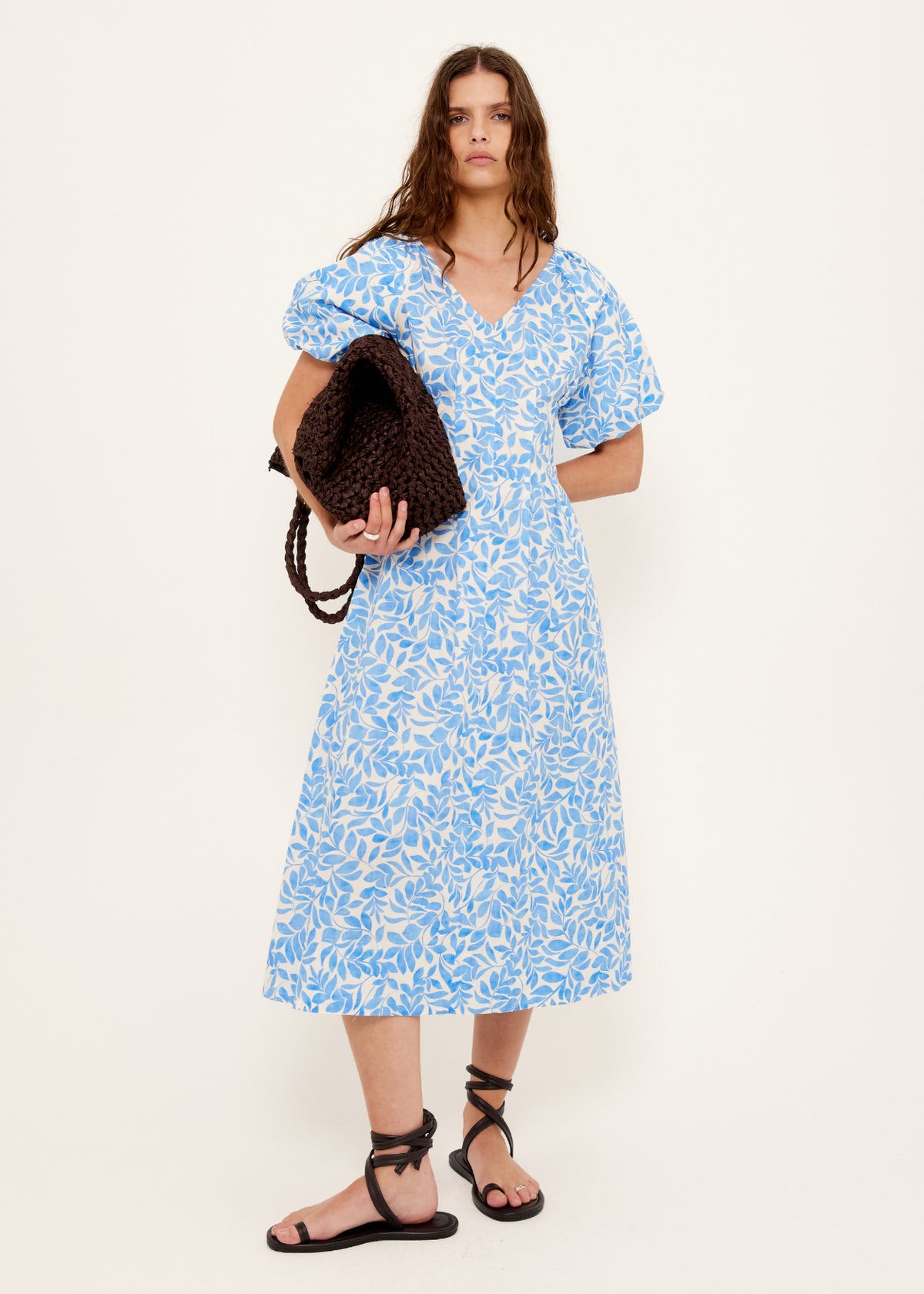 Model wearing Cotton Blue Leaf Print V-neck Midi Dress with a v-neckline with gathered bust seam and a short puff sleeves with elastic cuff.