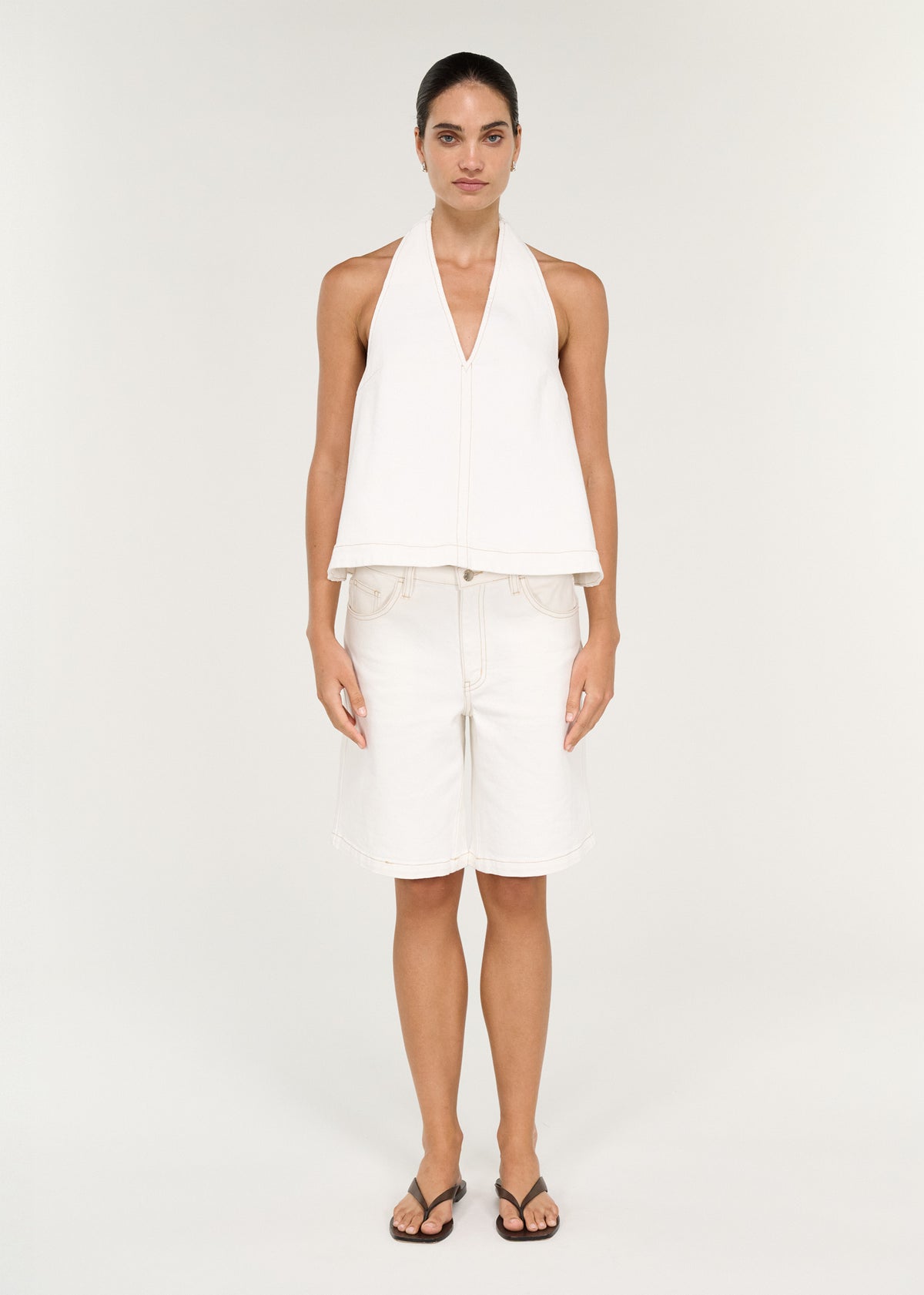 Model wearing Cotton Denim Halter Top in White with an open back and a branded button closure at back.